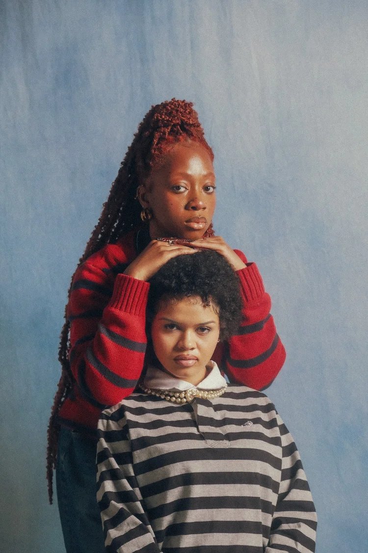 Two models in red and navy striped shirts pose against a blue backdrop in Polos and Varsities. Photography by Yonathan Mesfun.