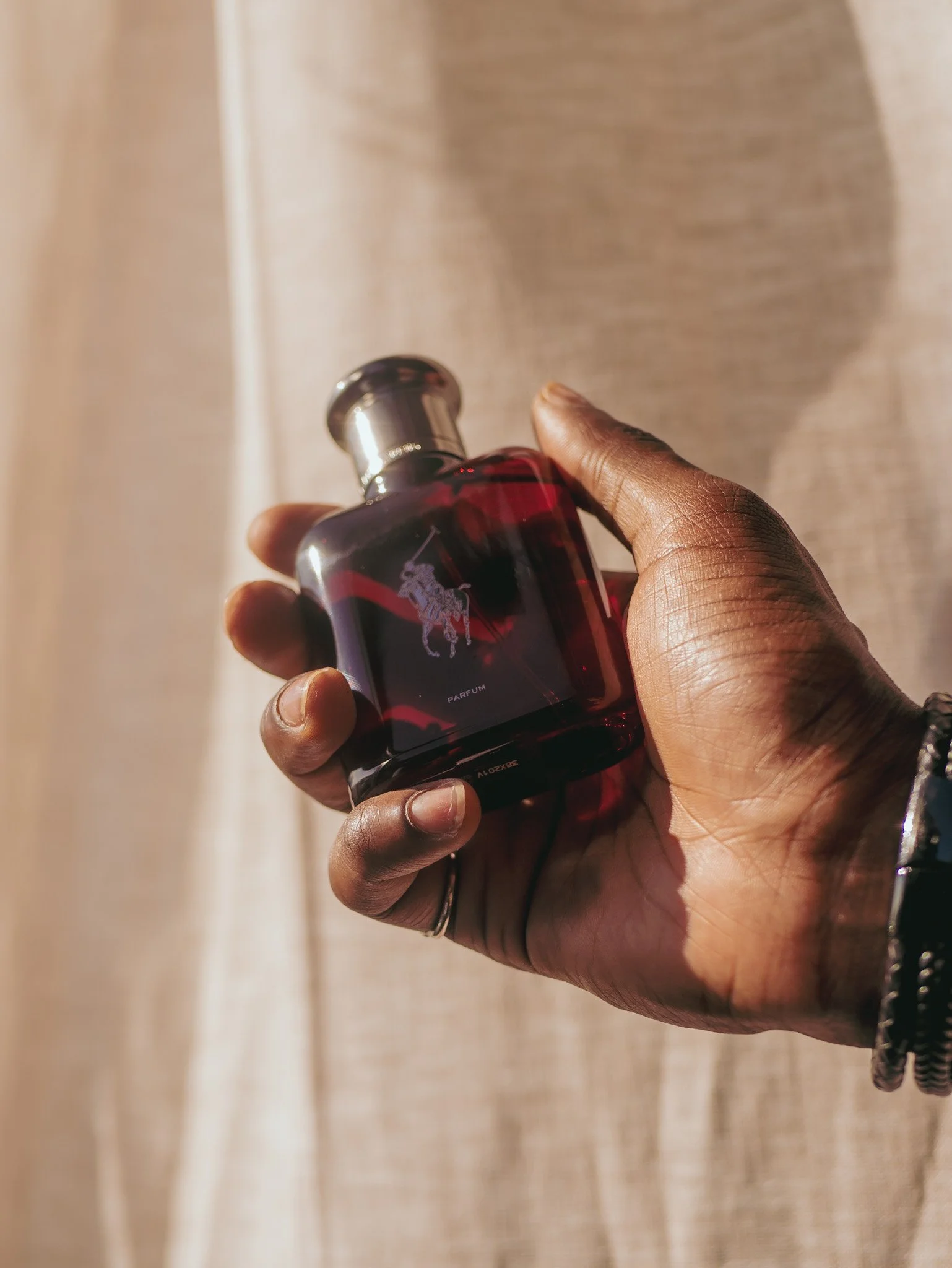 Close view of a hand holding a red Ralph Lauren Polo fragrance bottle in sunlight. Photography by Yonathan Mesfun.