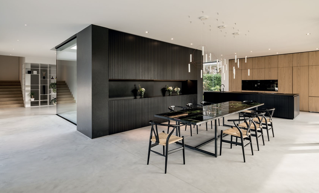Modern open-concept kitchen and dining area with black and wood cabinetry, a large dining table with black chairs, a black kitchen island, and contemporary pendant lighting.
