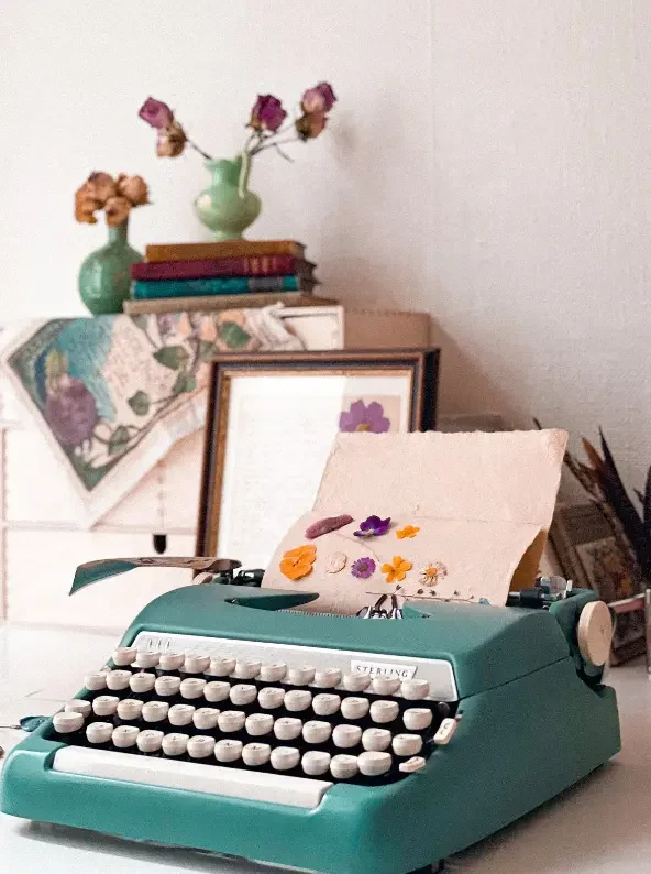 Máquina de escribir vintage turquesa con flores prensadas y libros, taller de escritura   creativa