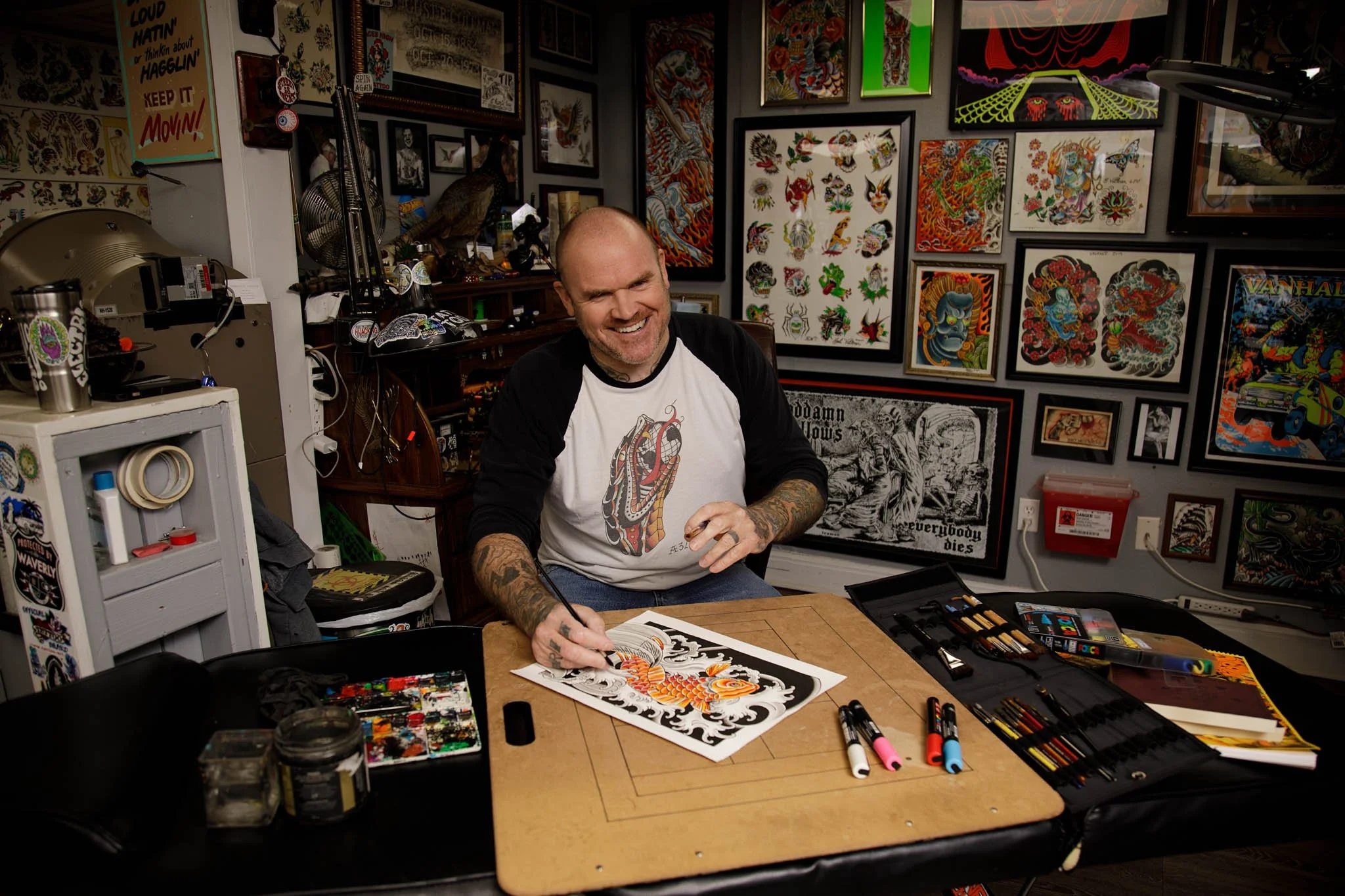 behind the scenes photo of tattoo artist at work station surrounded by artwork and art tools at electric wizard tattoo  / Photo by Erin Valkner Photography of New Braunfels, Texas. See more at www.erinvalknerphotography.com/blog