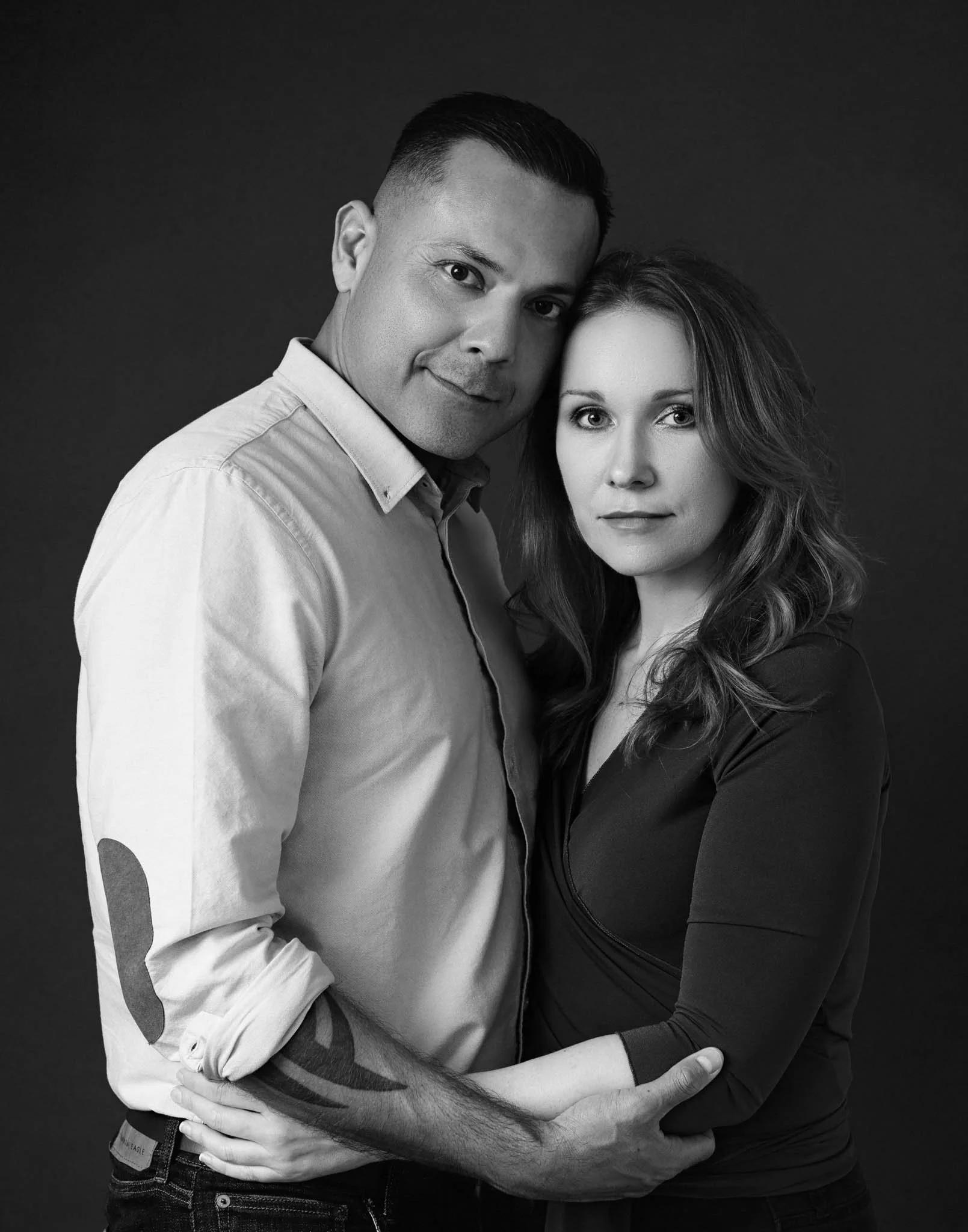 black and white portrait of couple in studio with dark background neutral relaxed expressions looking at camera / Photo by Erin Valkner Photography of New Braunfels, Texas. See more at www.erinvalknerphotography.com/blog
