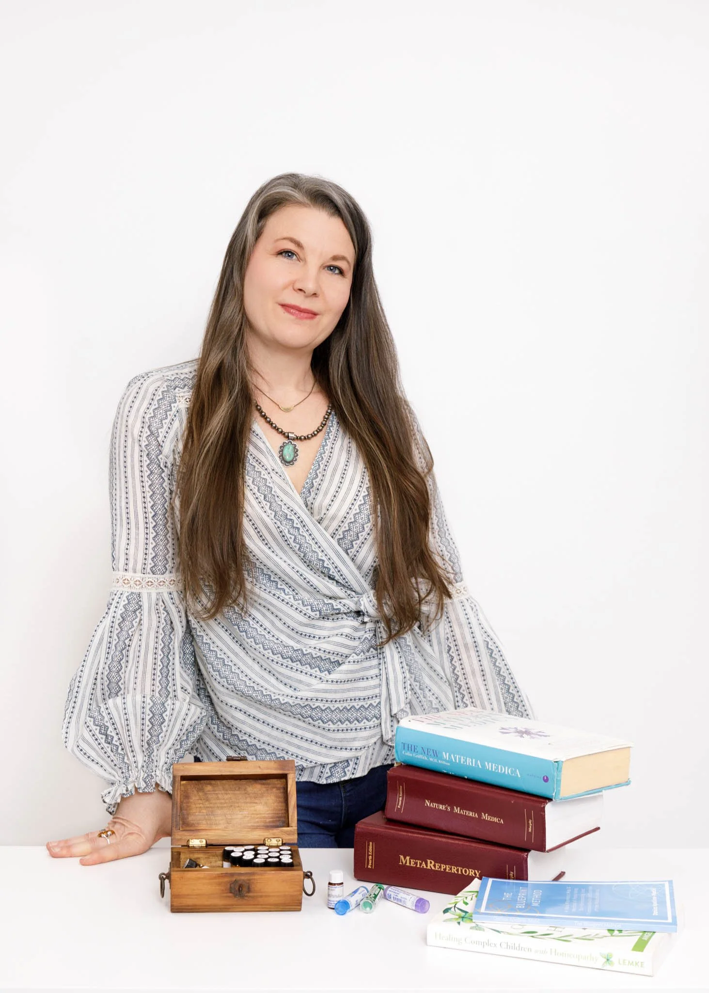 woman leaning on desk with variety of homeopathic items such as books vials, box and informational materials / Photo by Erin Valkner Photography of New Braunfels, Texas. See more at www.erinvalknerphotography.com/blog
