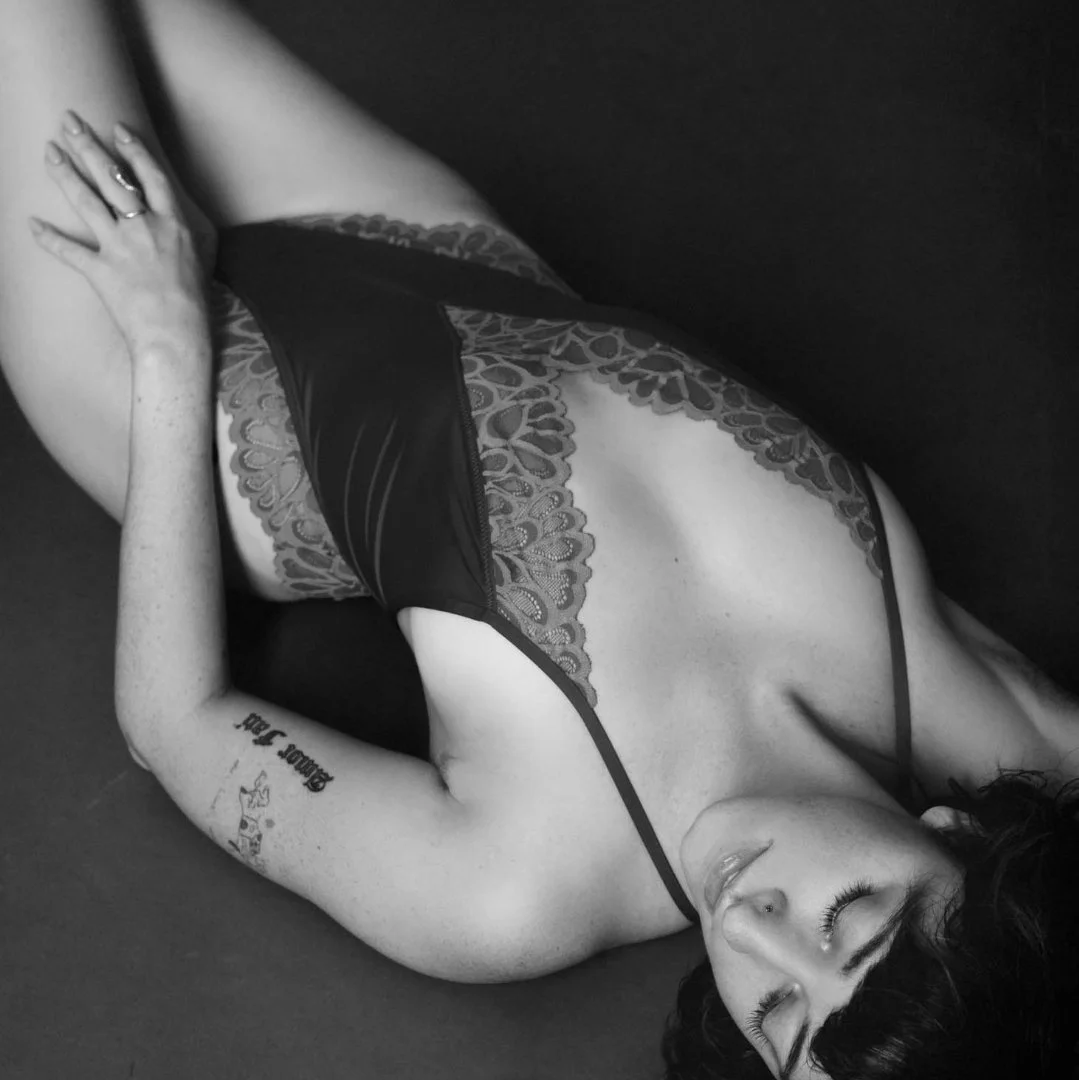 black and white boudoir portrait lying down pose woman wearing bodysuit with lace and tatoo on arm / Photo by Erin Valkner Photography of New Braunfels, Texas. See more at www.erinvalknerphotography.com/blog