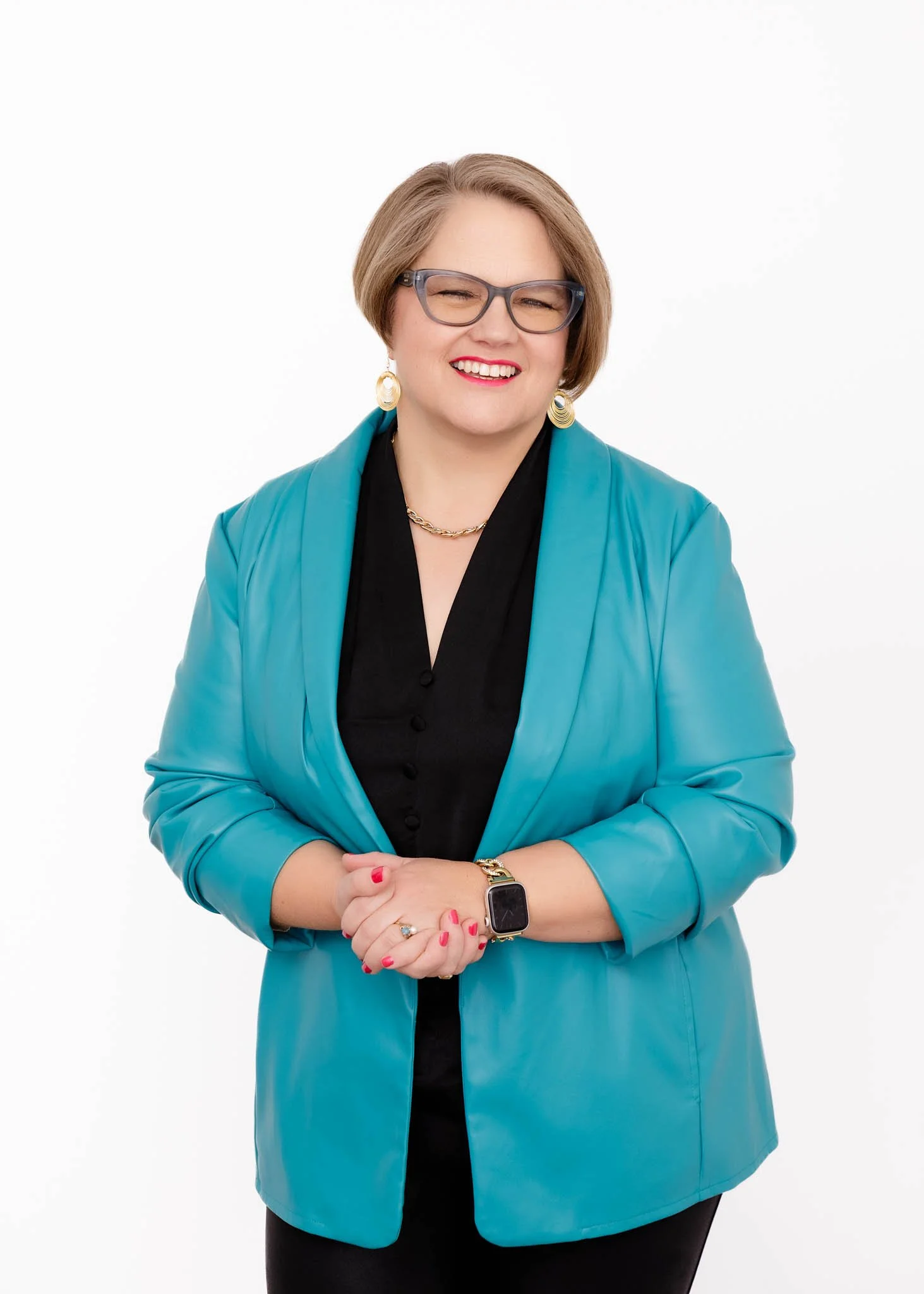 woman with glasses and short blond hair smiling wearing turquoise suit jacket and black blouse and pants with bold lip color and earrings for standing post branding headshot photo with white background