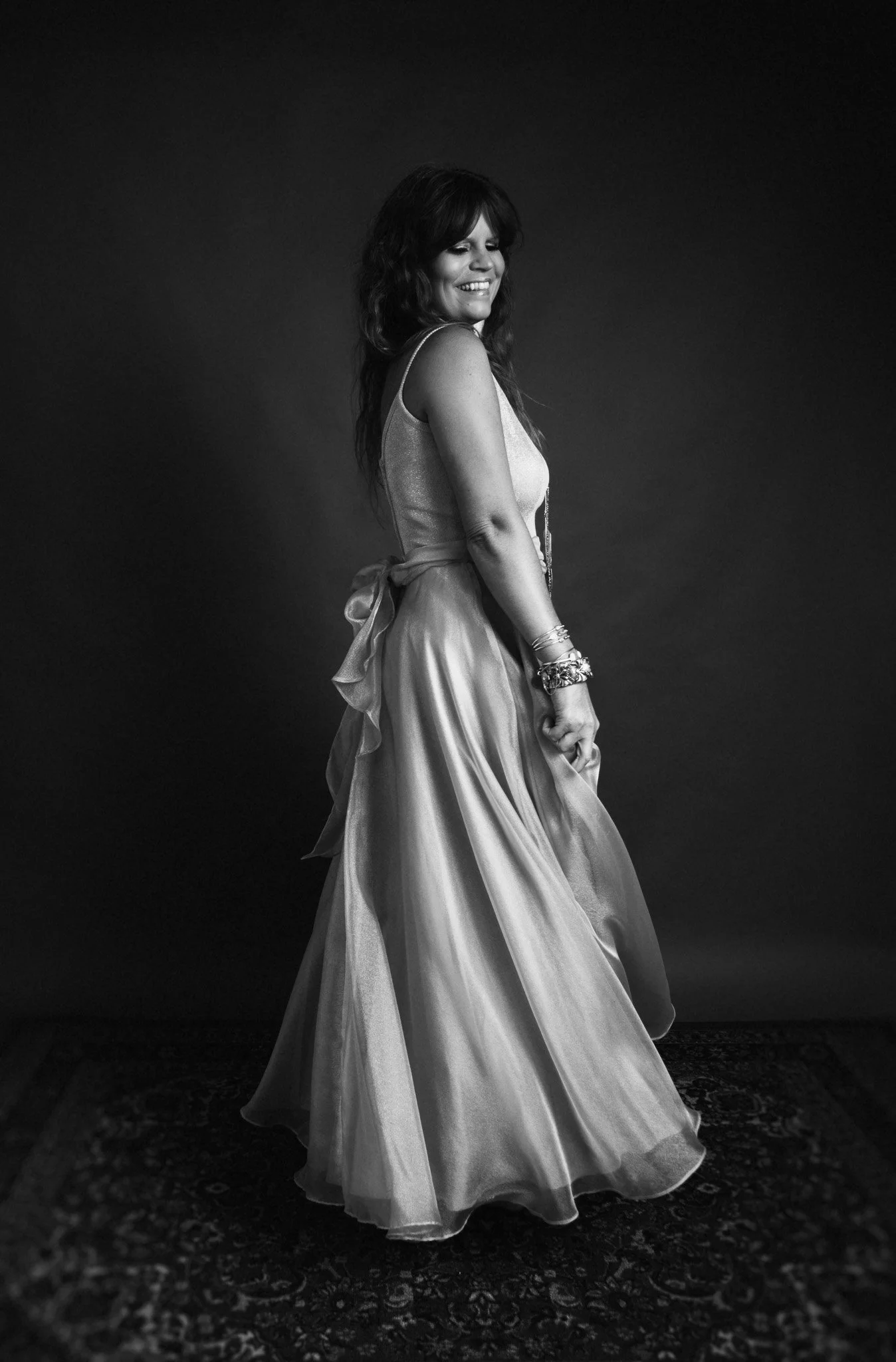 black and white portrait of woman with long dark hair in twirly dress smiling in studio dark backdrop / Photo by Erin Valkner Photography of New Braunfels, Texas. See more at www.erinvalknerphotography.com/blog