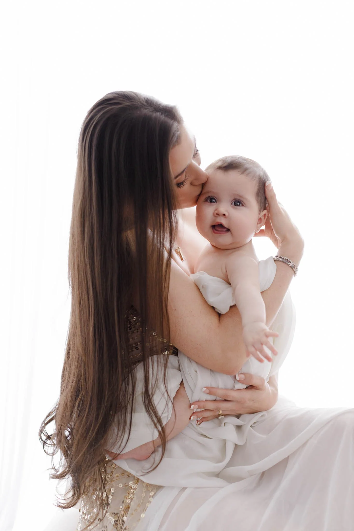 mom and baby girl in front of backlit background light color dress and sheer fabric wrap / Photo by Erin Valkner Photography of New Braunfels, Texas. See more at www.erinvalknerphotography.com/blog