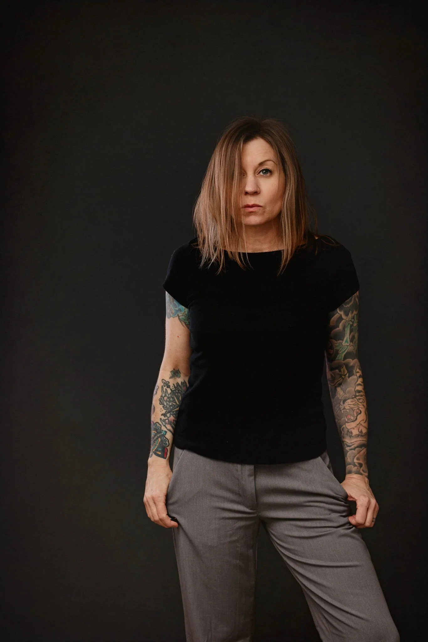 woman with tattoos and blond grey hair black shirt grey trousers on dark grey background / Photo by Erin Valkner Photography of New Braunfels, Texas. See more at www.erinvalknerphotography.com/blog