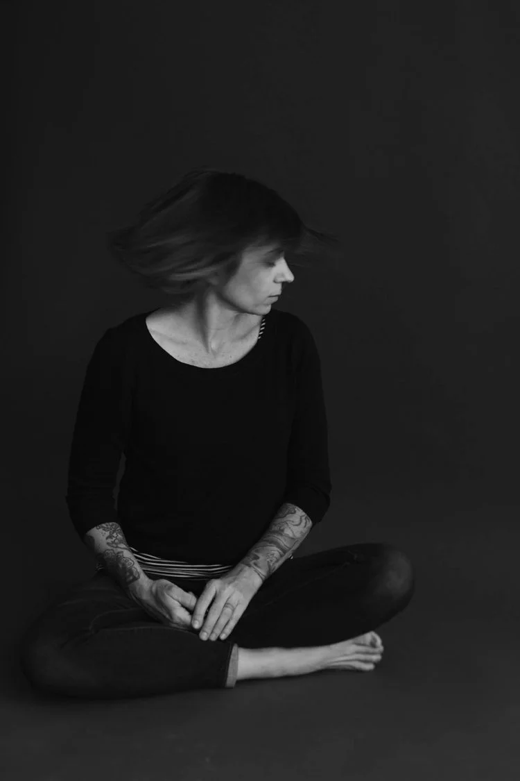black and white raw portrait of woman sitting cross legged with hands in lap, hair swish looking away from camera dark backdrop in studio / Photo by Erin Valkner Photography of New Braunfels, Texas. See more at www.erinvalknerphotography.com/blog