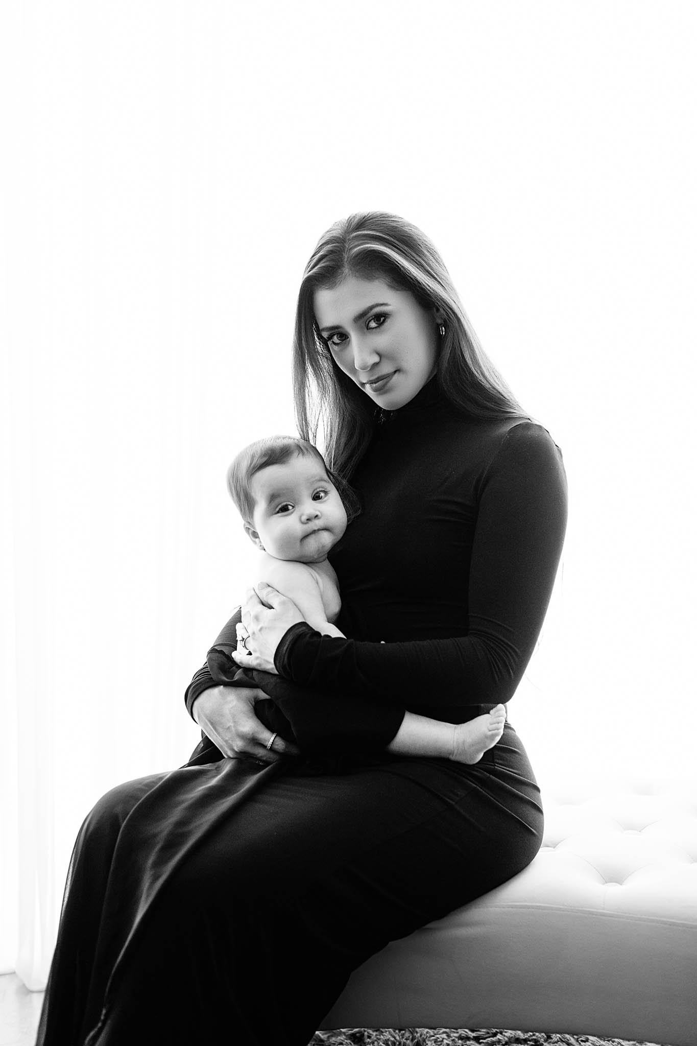 black and white photo of mom wearing black turtleneck and baby sitting in front of backlit window in studio / Photo by Erin Valkner Photography of New Braunfels, Texas. See more at www.erinvalknerphotography.com/blog
