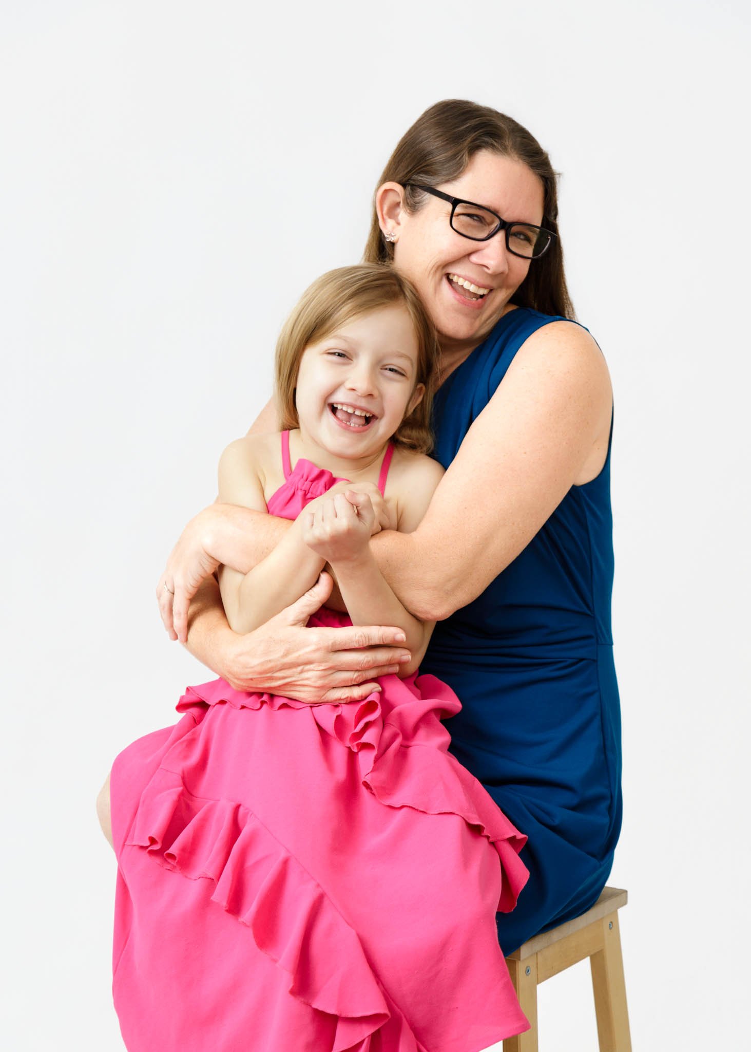 mom and daughter smiling embrace sitting on stool white backdrop / Photo by Erin Valkner Photography of New Braunfels, Texas. See more at www.erinvalknerphotography.com/blog