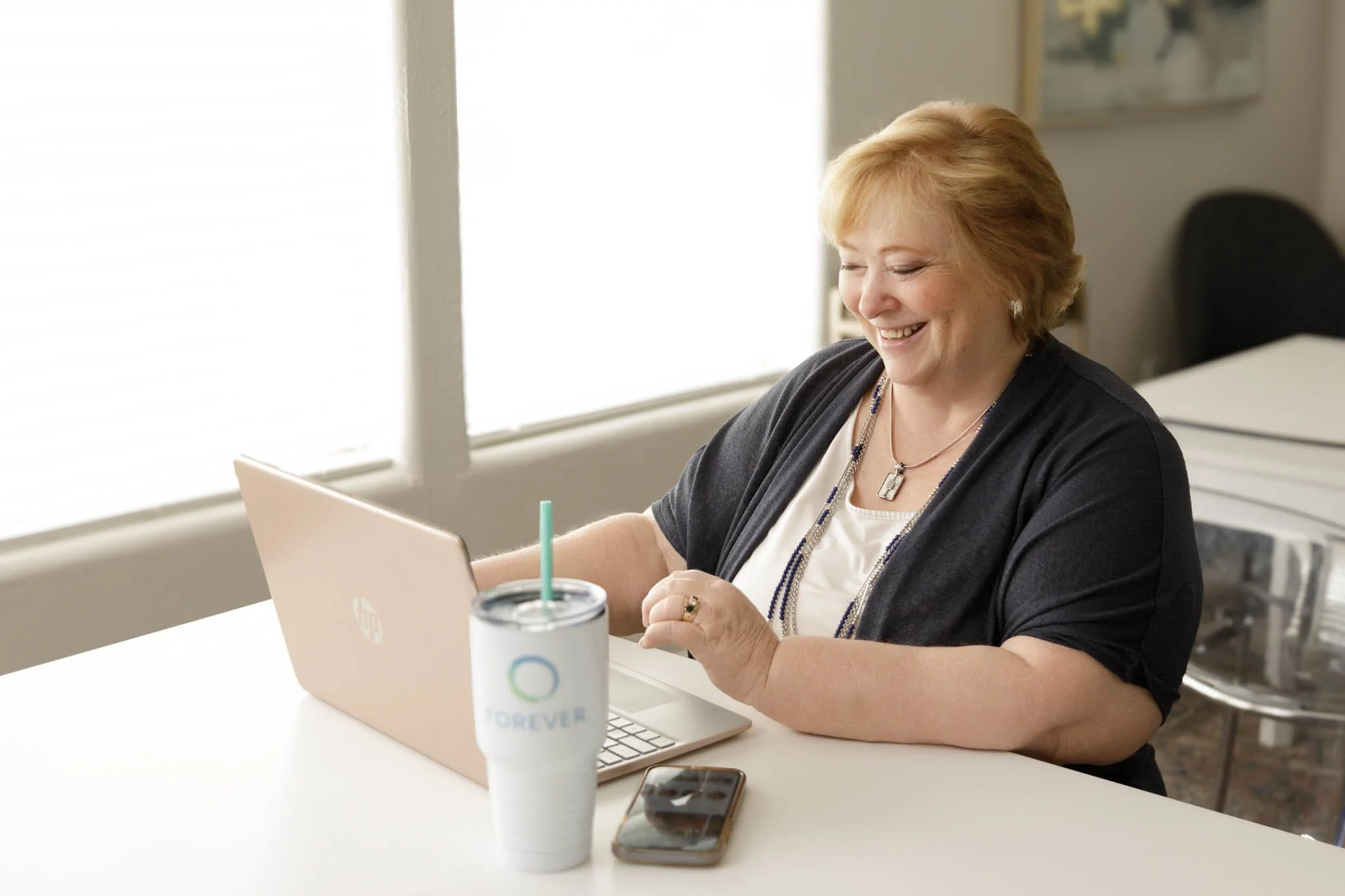 branding photo of woman smiling working at desk looking at laptop with phone and drink on desk  / Photo by Erin Valkner Photography of New Braunfels, Texas. See more at www.erinvalknerphotography.com/blog