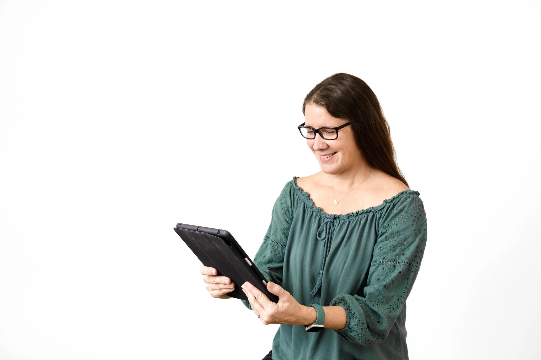 woman wearing glasses and green top long brown hair with tablet white background / Photo by Erin Valkner Photography of New Braunfels, Texas. See more at www.erinvalknerphotography.com/blog
