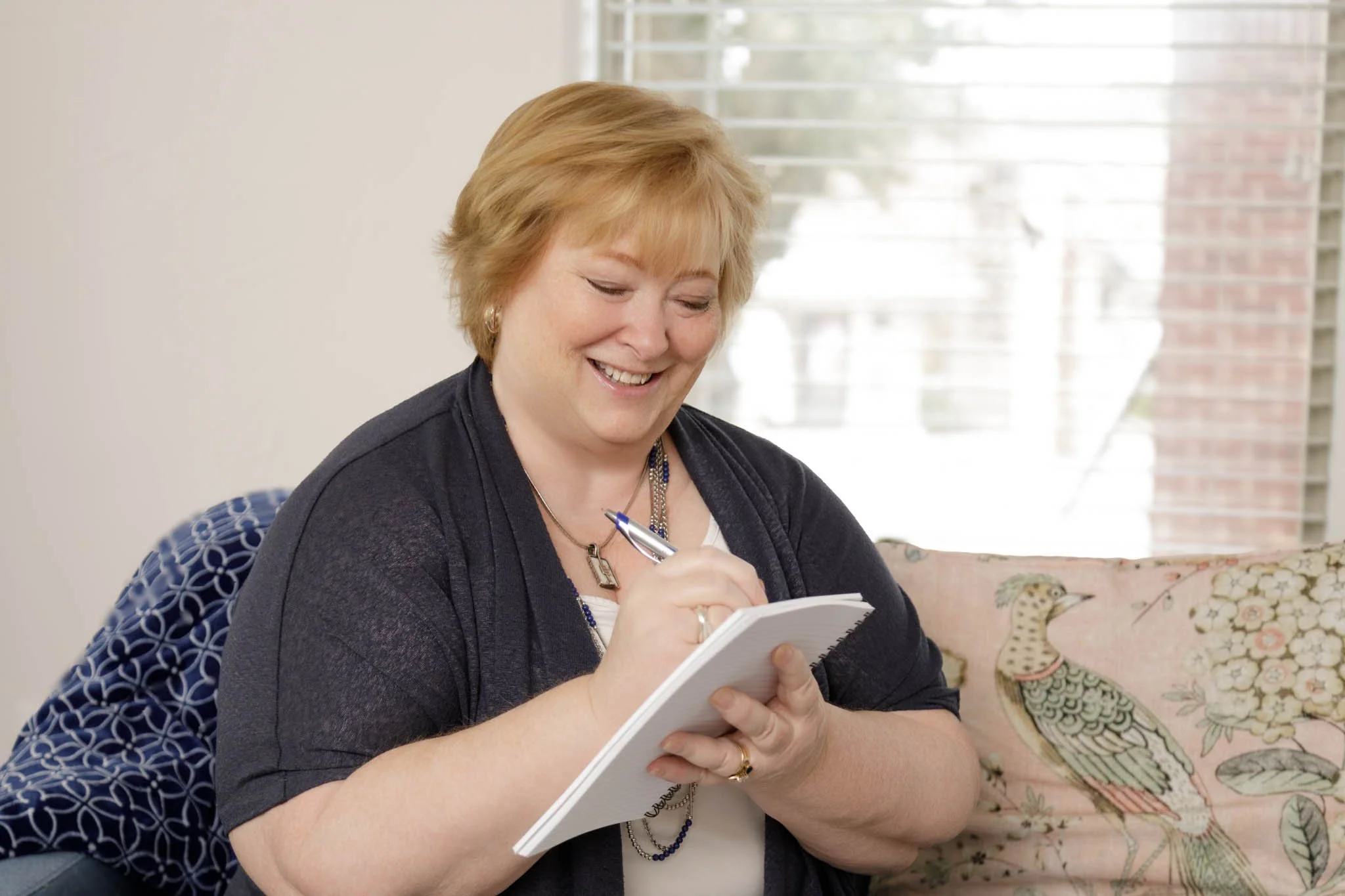branding photo of woman sitting on sofa writing in notebook smiling looking at work  / Photo by Erin Valkner Photography of New Braunfels, Texas. See more at www.erinvalknerphotography.com/blog