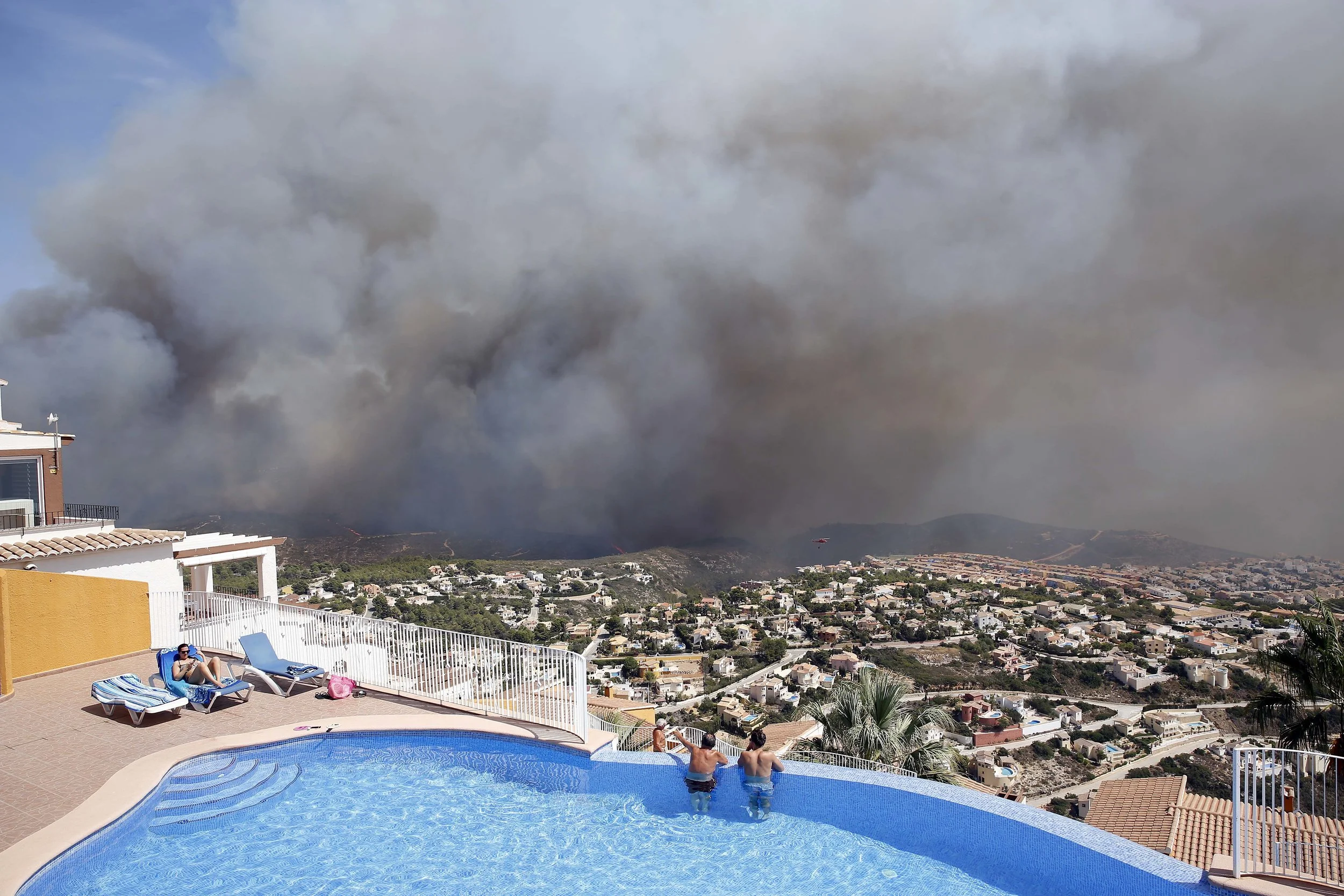 Two men look out from a swimming pool at a wildfire as it burns nearby in eastern Spain. Scientists say southern Spain will become desert and deciduous forests will vanish from much of the Mediterranean basin unless global warming is reined in sharply. They concluded that any warming above 2 degrees Celsius would cause changes not seen in 10,000 years. (AP Photo/Alberto Saiz, file)