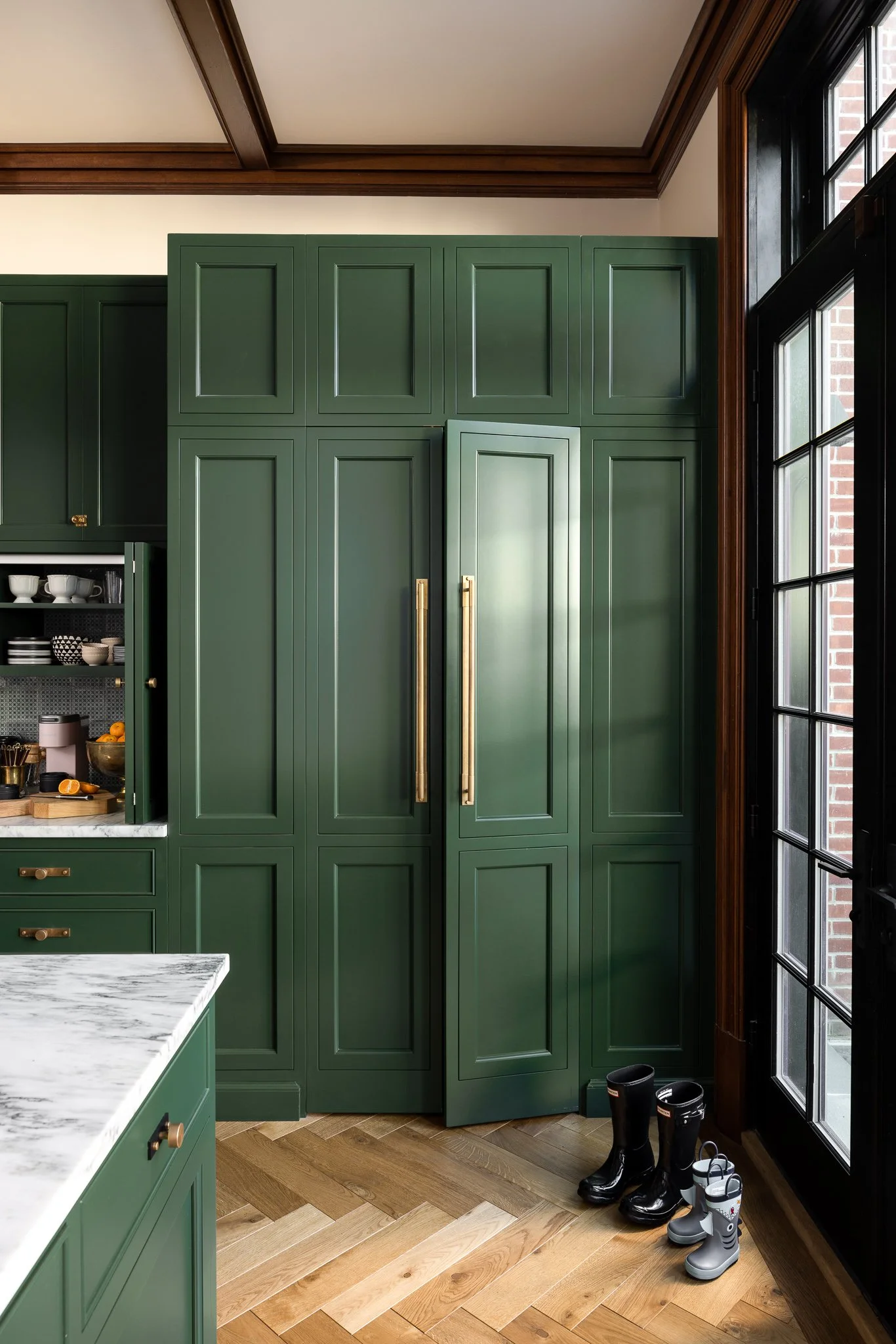 Custom green kitchen pantry cabinetry with brass pulls and herringbone wood flooring in a Philadelphia row home kitchen remodel by J.THOM