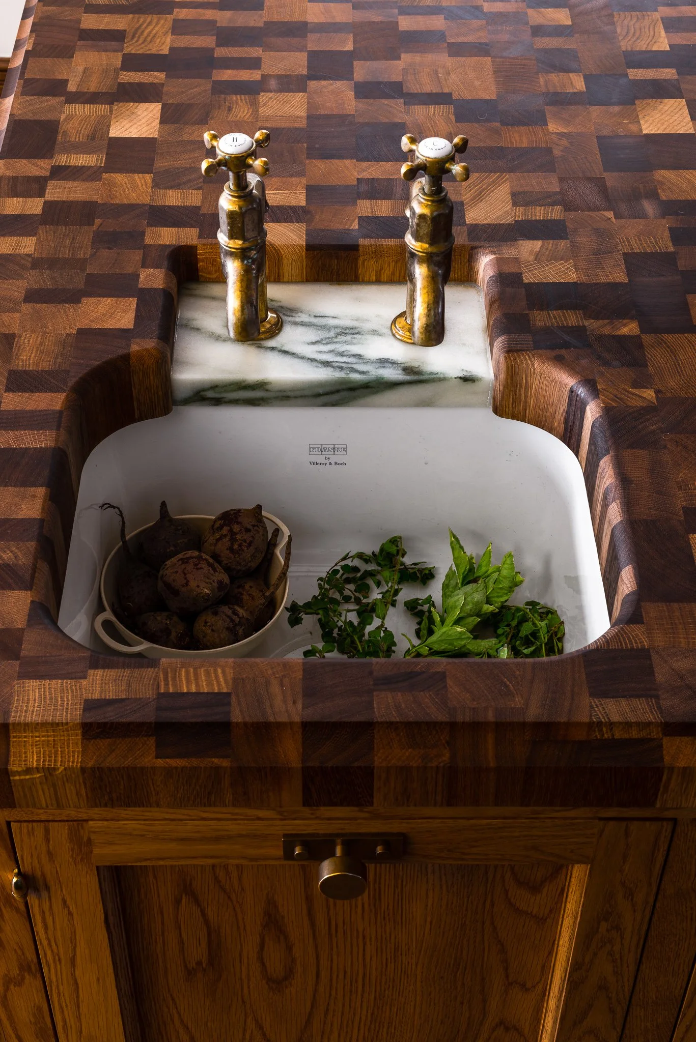 Fireclay farmhouse sink with end-grain butcher block countertop and aged brass bridge faucet in custom kitchen design