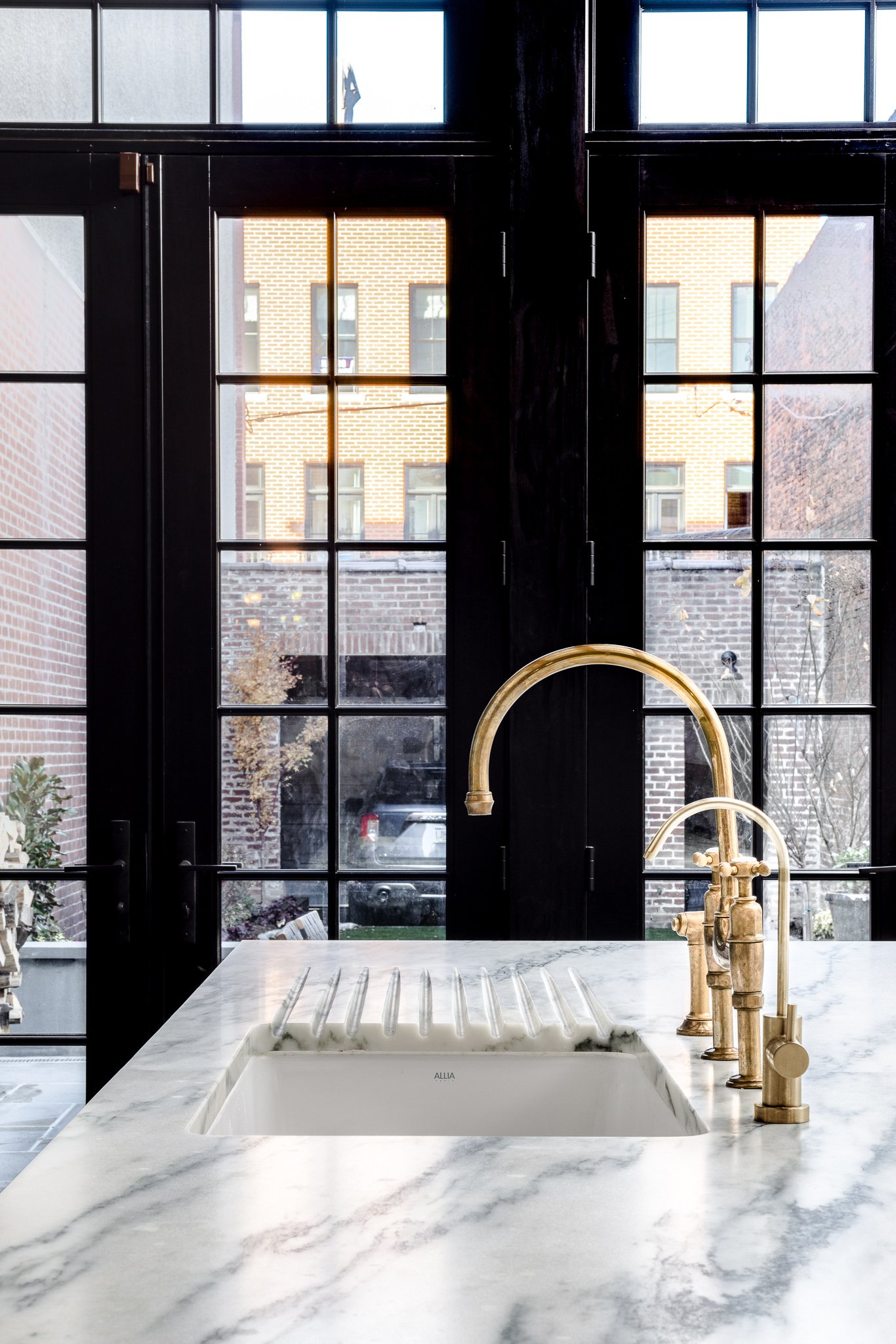 Marble countertop with integrated drainboard sink and aged brass bridge faucet in custom Philadelphia kitchen remodel