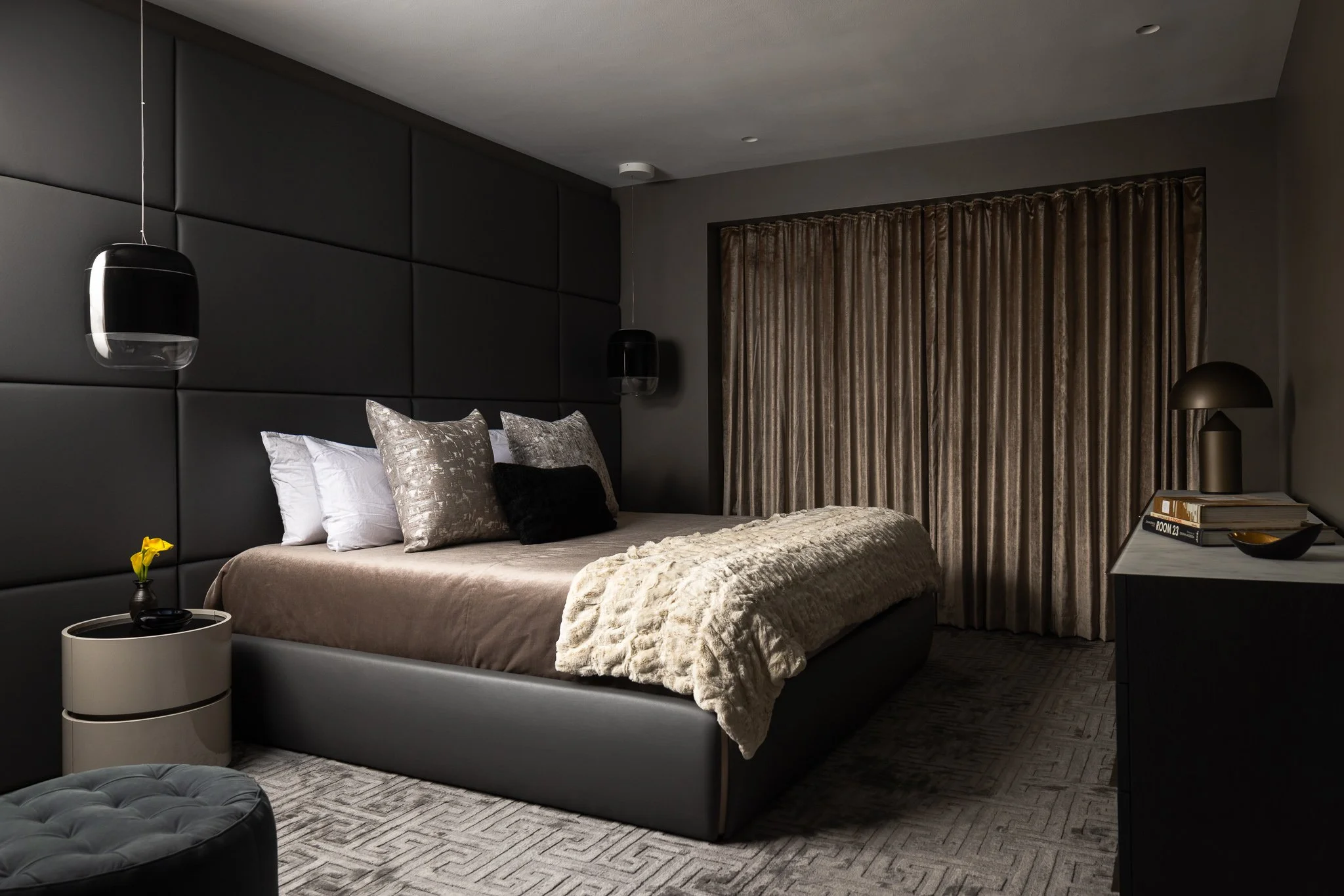 primary bedroom with upholstered wall panels silk rug and pendant lighting