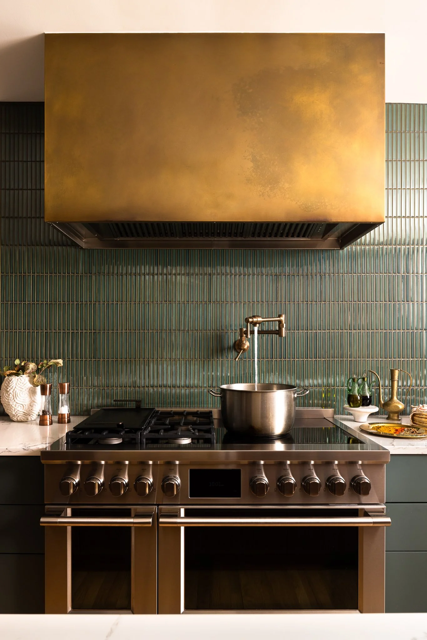 kitchen design with custom cabinetry brass hood gas range pot filler textured backsplash warm lighting