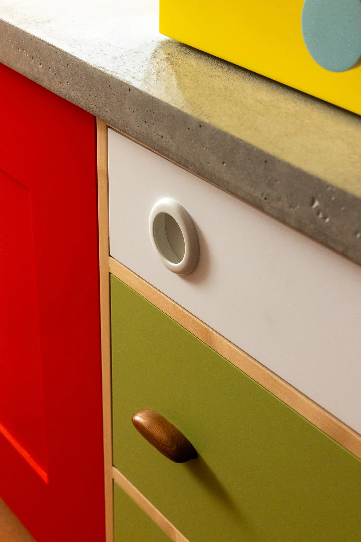 Colorful cabinet fronts with oversized hardware and playful custom detailing including a concrete countetop.