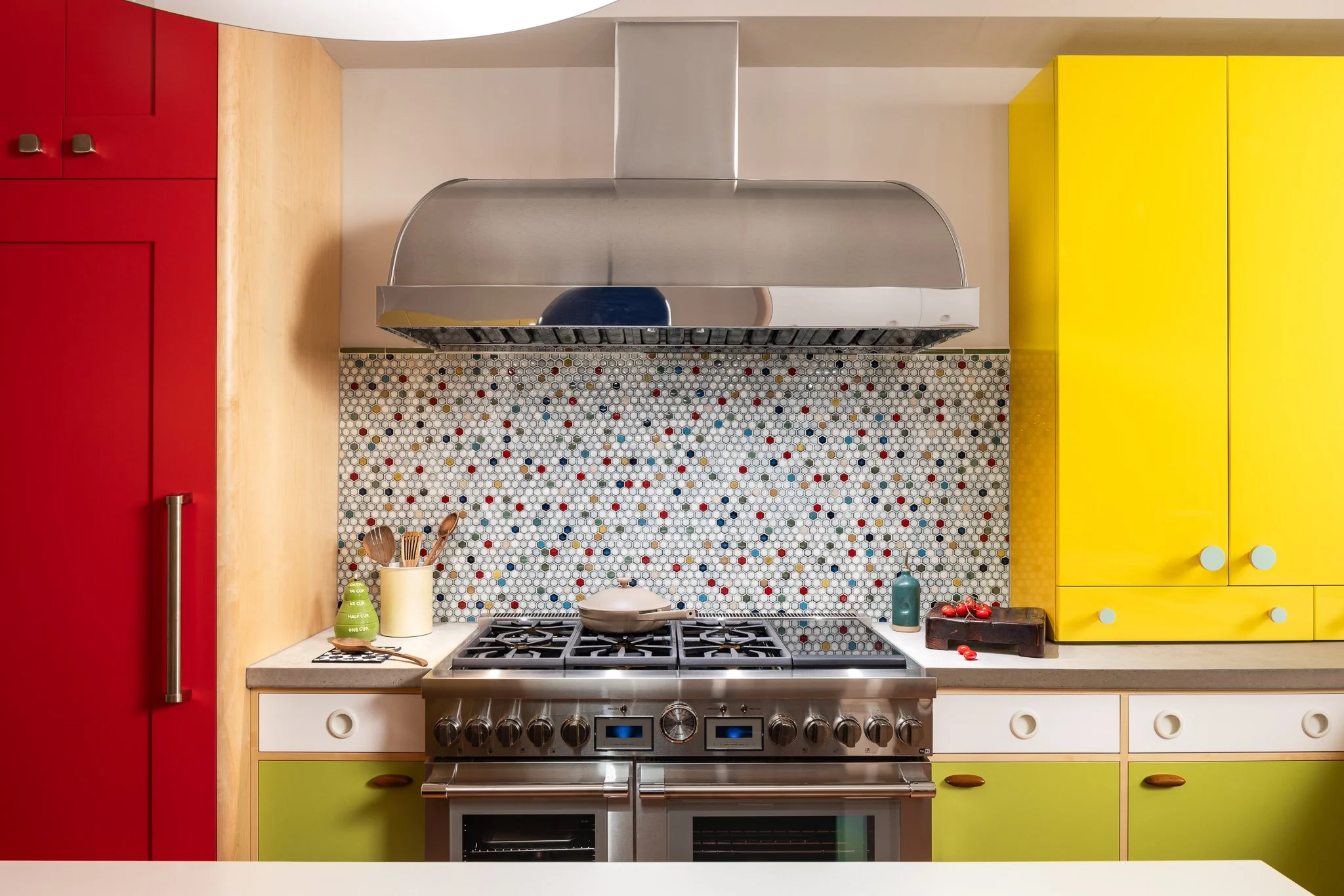 Stainless steel hood and 48-inch induction-gas range framed by colorful custom cabinetry.