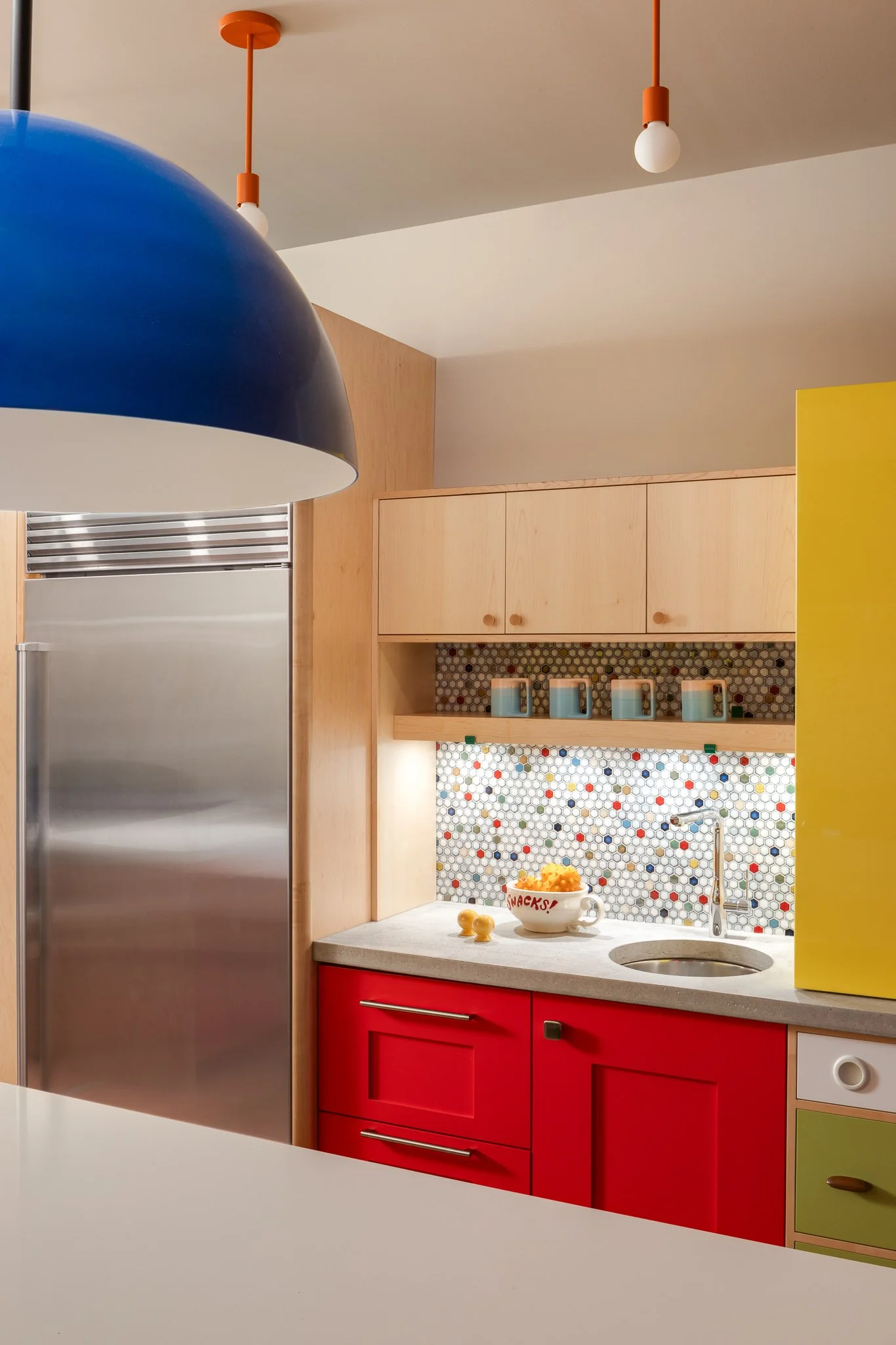 Beverage center with maple cabinetry, a concrete countertop, chrome faucet, and colorful tile backsplash.