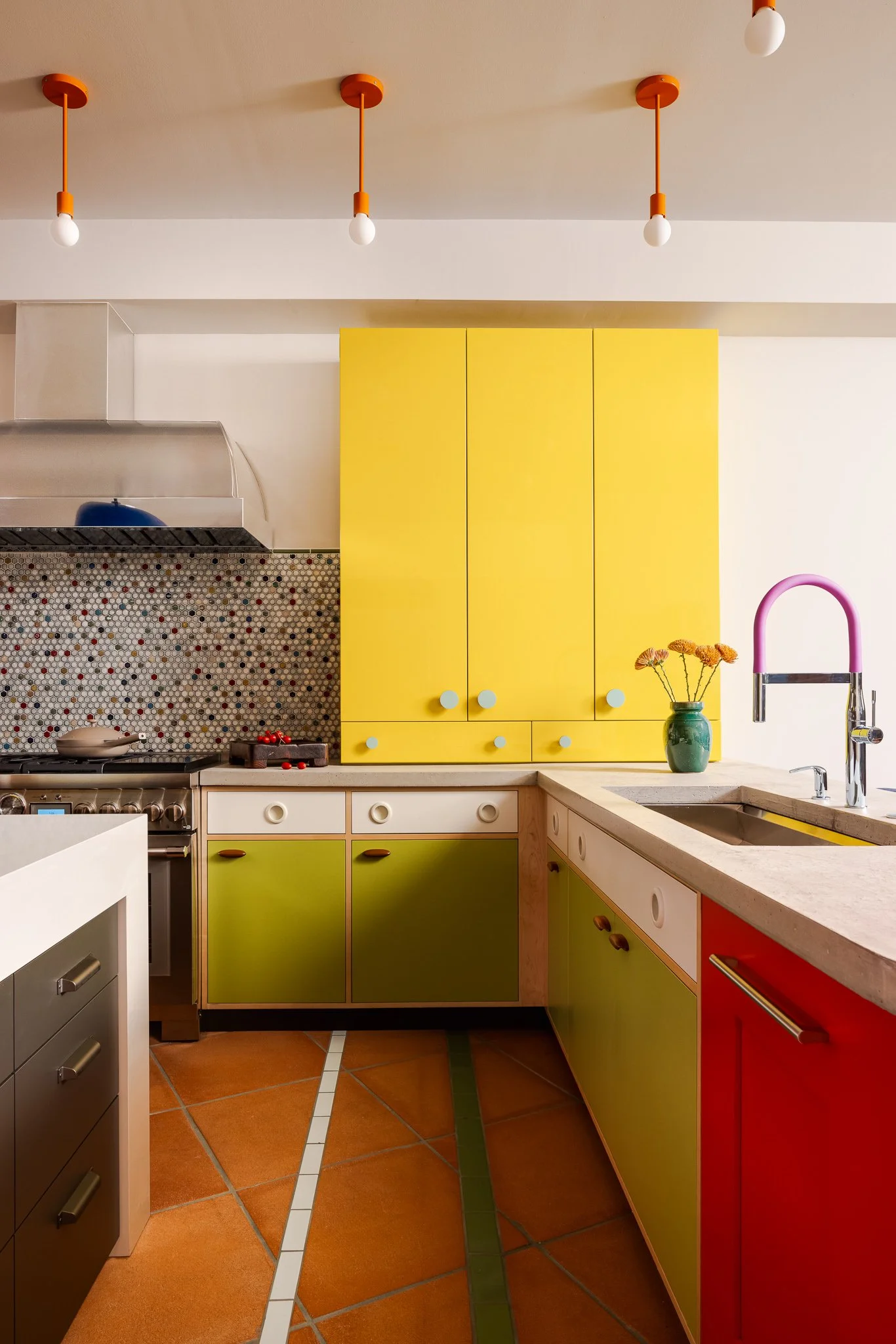 Colorful kitchen with high-gloss yellow cabinetry, a 48-inch range, concrete countertops, and terracotta tile flooring.