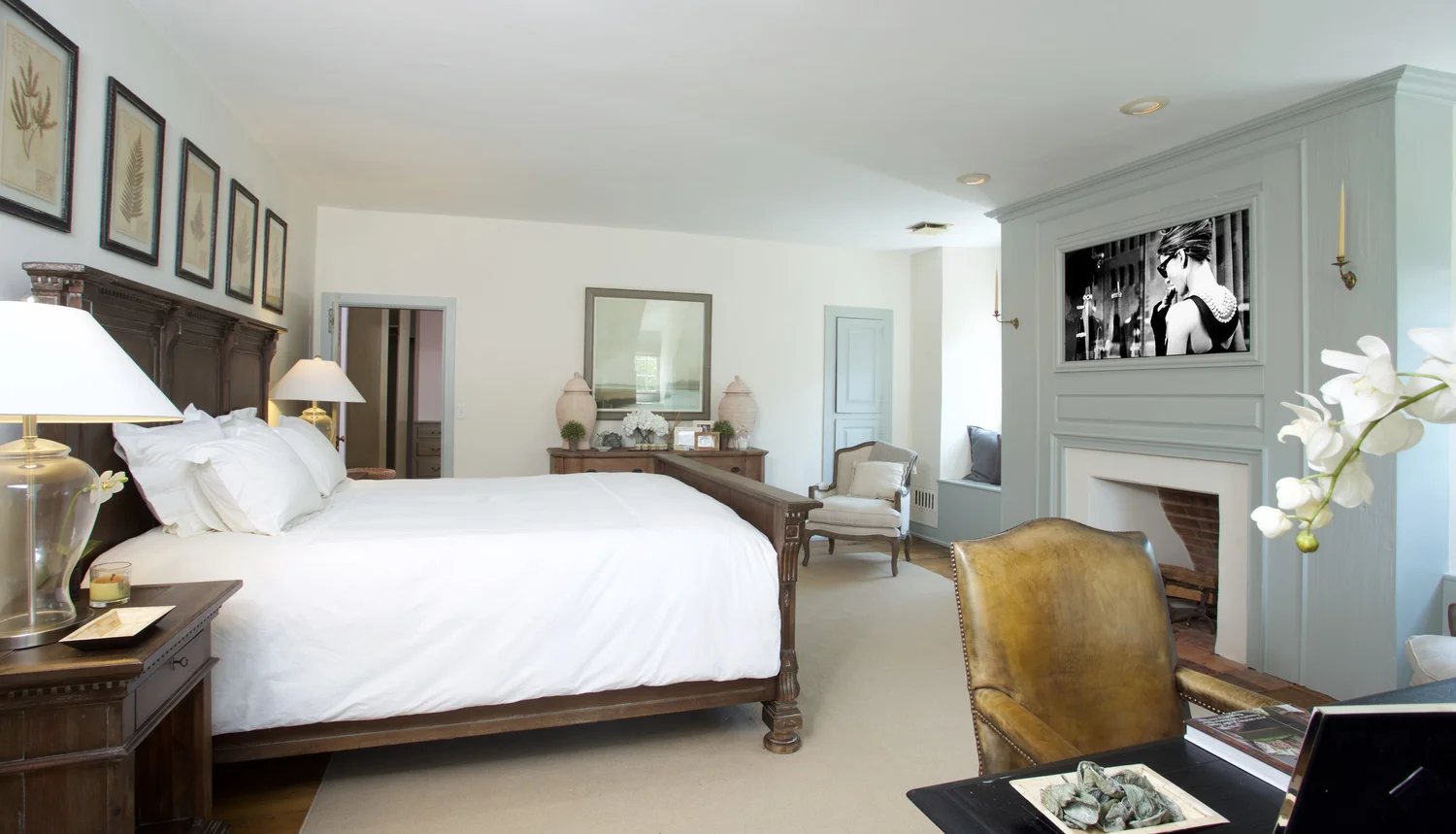 The primary suite with a carved dark-wood bed, crisp white linens, and framed botanical prints