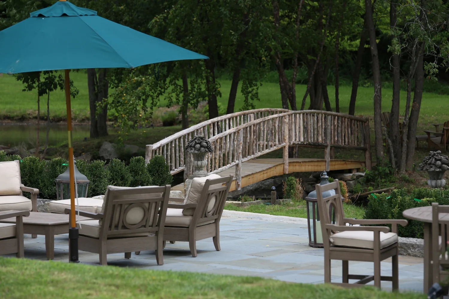 A bluestone terrace by the pond with a hand-built rustic wooden bridge crossing the water