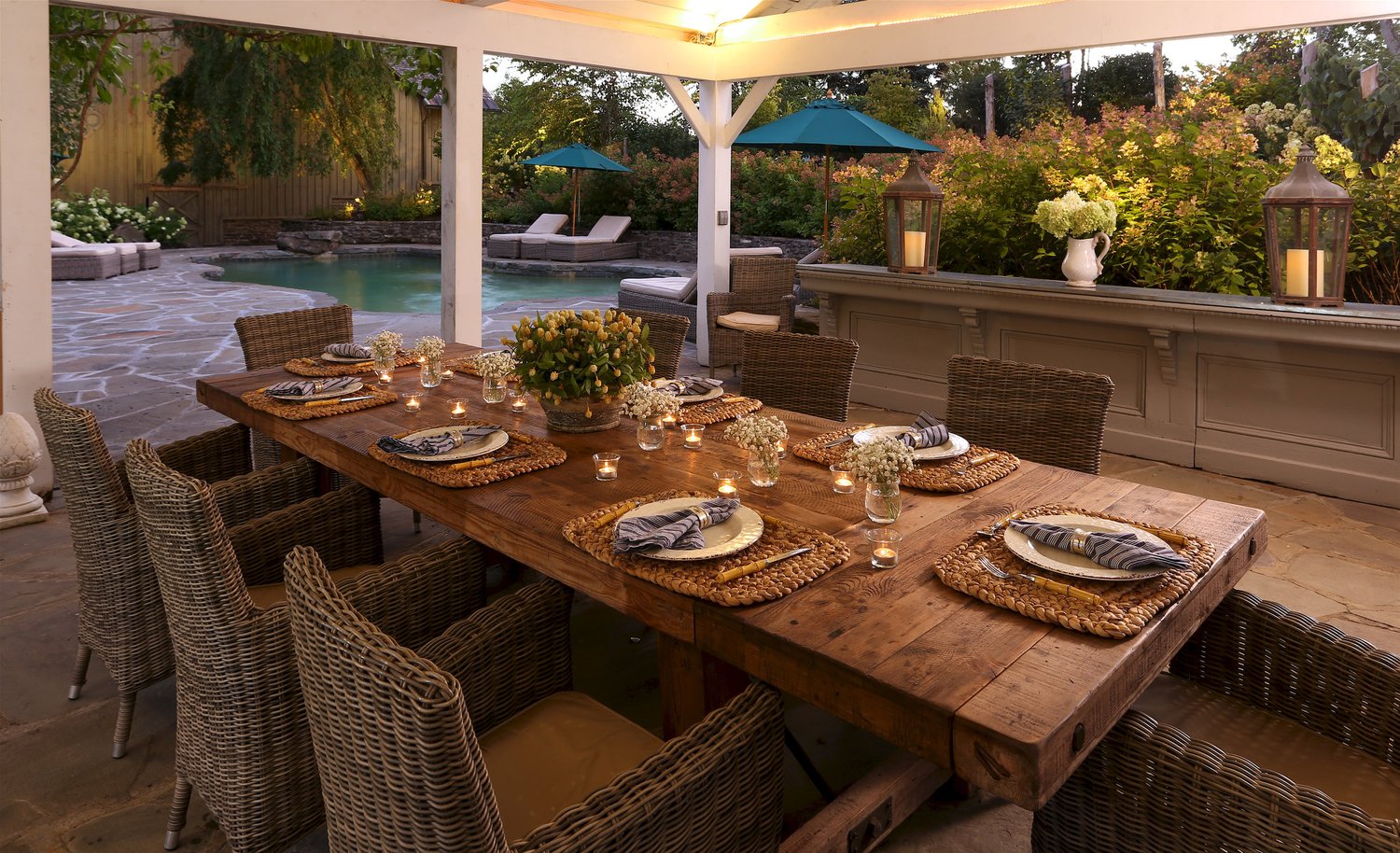A covered bluestone pavilion set for dinner at dusk, overlooking the heated pool with teal umbrellas