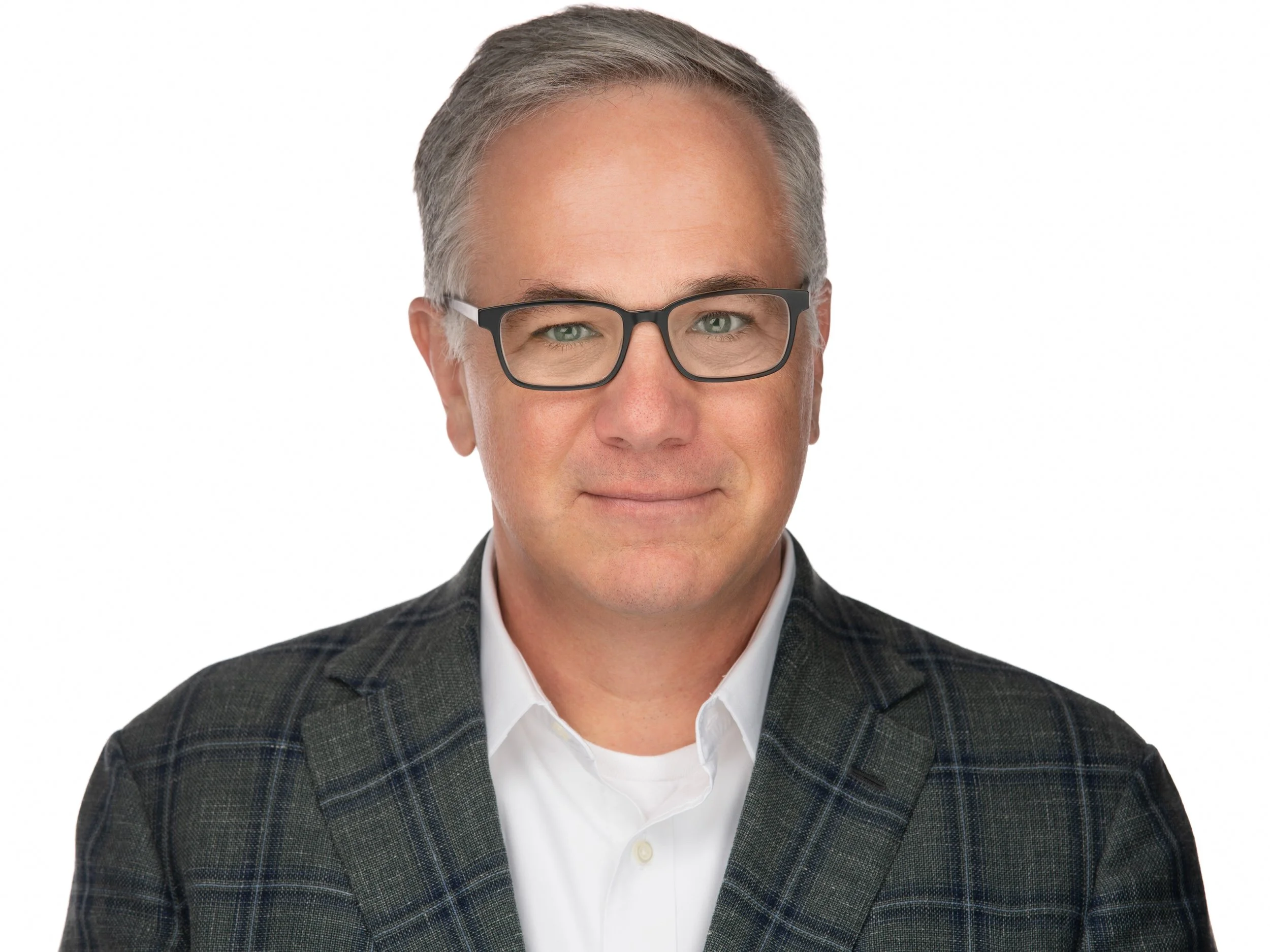 A man with dark hair, glasses, and a light complexion wearing a navy plaid suit, white shirt, and a yellow patterned tie against a gray background.