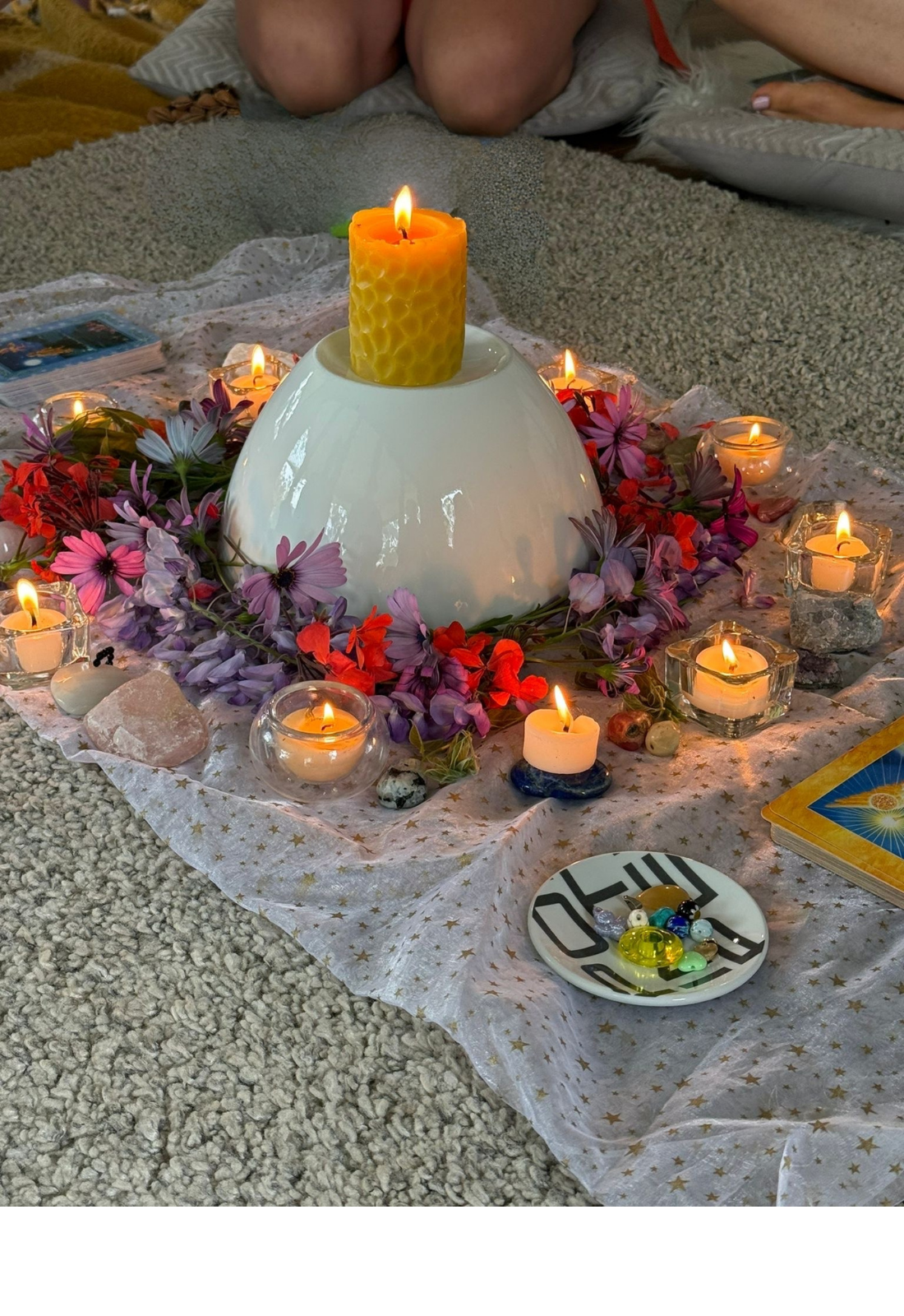 A spiritual altar with candles, flowers, and crystals on a star-patterned cloth, with angel and goddess cards for a special Mothers' Blessing full of ritual, care, love, wisdom, friends and family. Facilitated by Hats at Pink Flamingo Postpartum