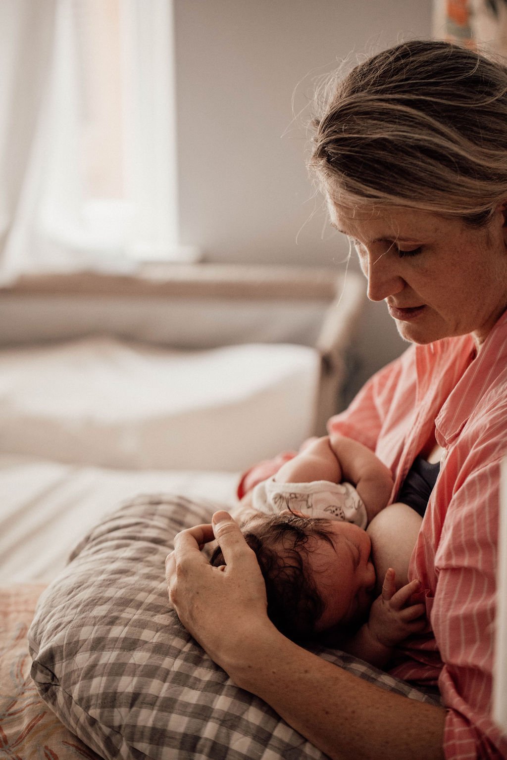 A woman breastfeeding a newborn baby lying on a pillow, in a sunlit room. Postpartum Doula Care Packages. The right care for a calm, joyful and supported postpartum. Sydney's Eastern Suburbs