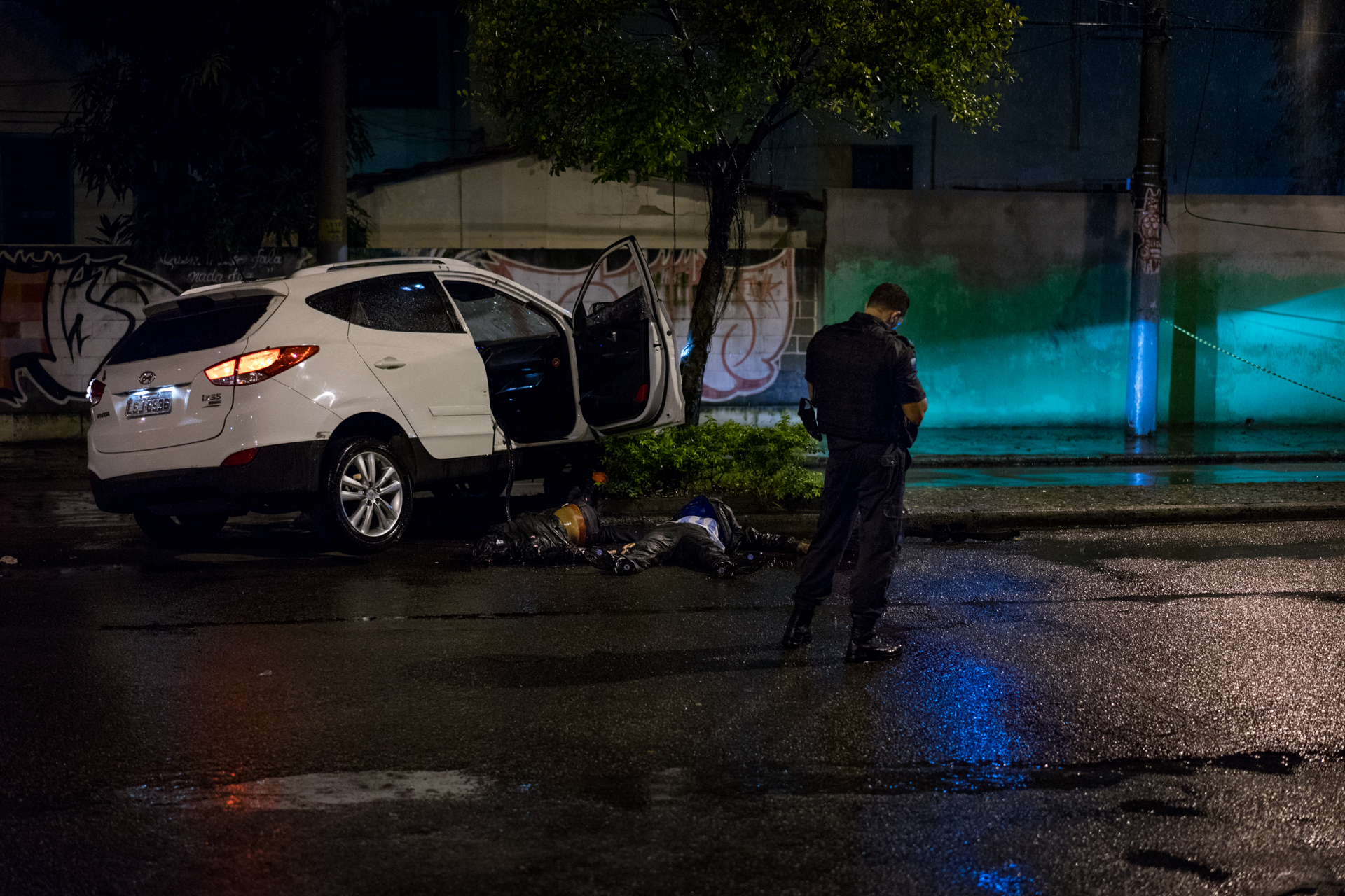 A Brazilian police officer stands watch over two alleged gang members shot by police after they ran a checkpoint 4, April 2018.