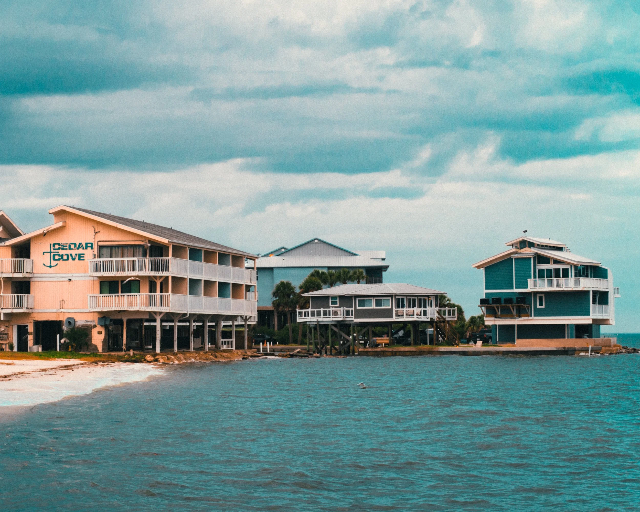 Colorful waterfront houses on stilts over the water under a cloudy sky in Cedar Key, FL.