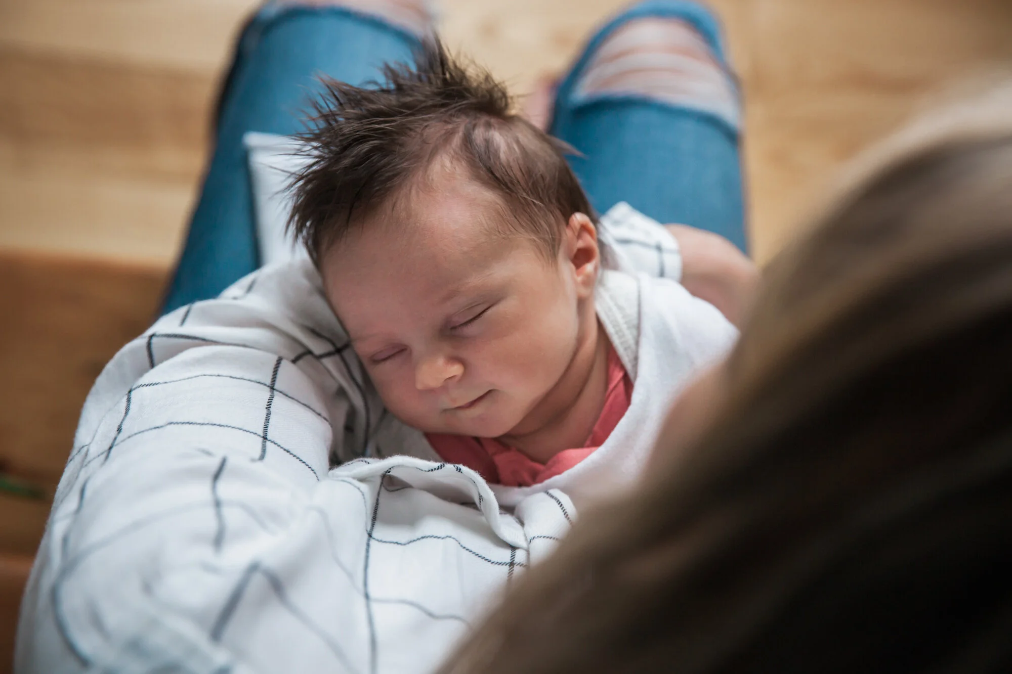 Photograph taken from over mother's shoulder. Mother holds baby, who sleeps in her arms with face toward the camera.
