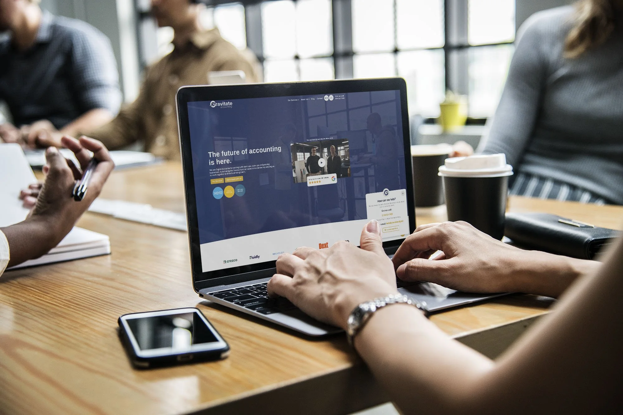 People sitting at a table in a meeting room, with a laptop displaying a website about accounting software.