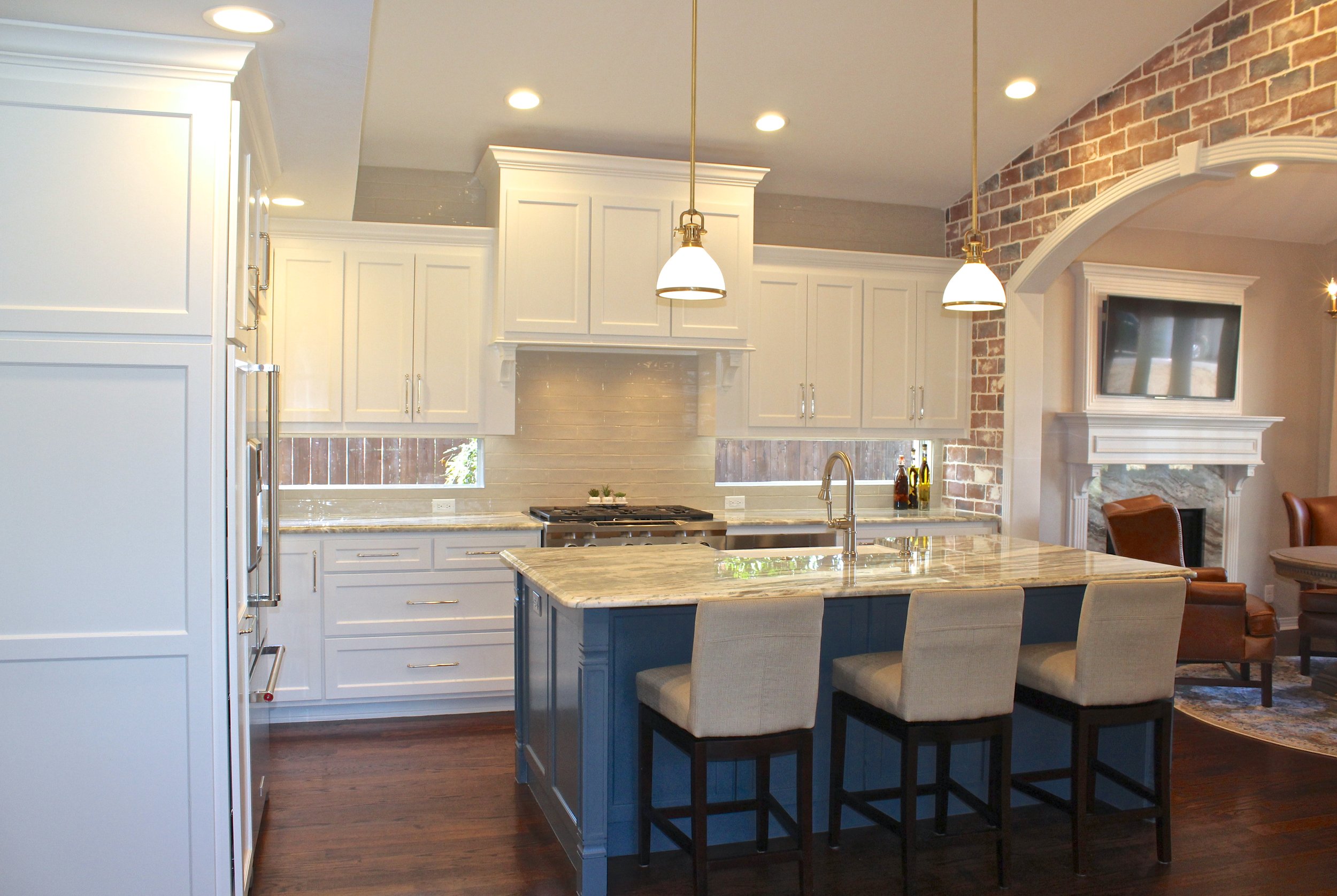 After: Large island with seating, antique brass fixtures, thoughtful design, brick archway, custom fireplace hearth