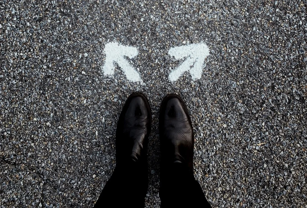 Downward shot of shoes standing in front of two directional arrows. Source: Unsplash