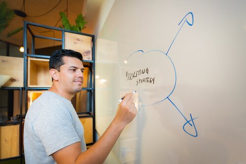 Man writing “marketing strategy” on whiteboard. Image credit: Unsplash