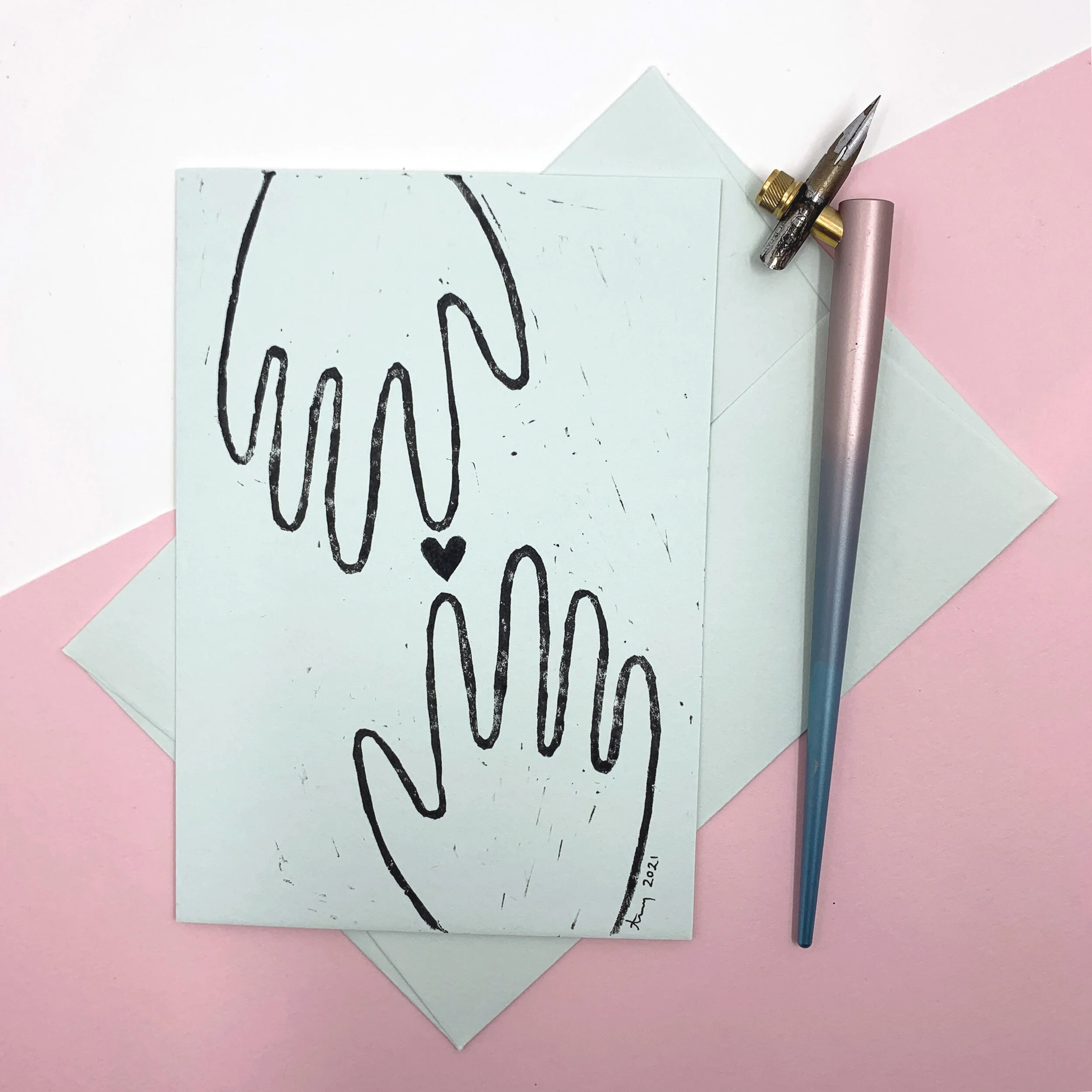 Green postcard with black linocut print. Print displays two hands and a heart between them.