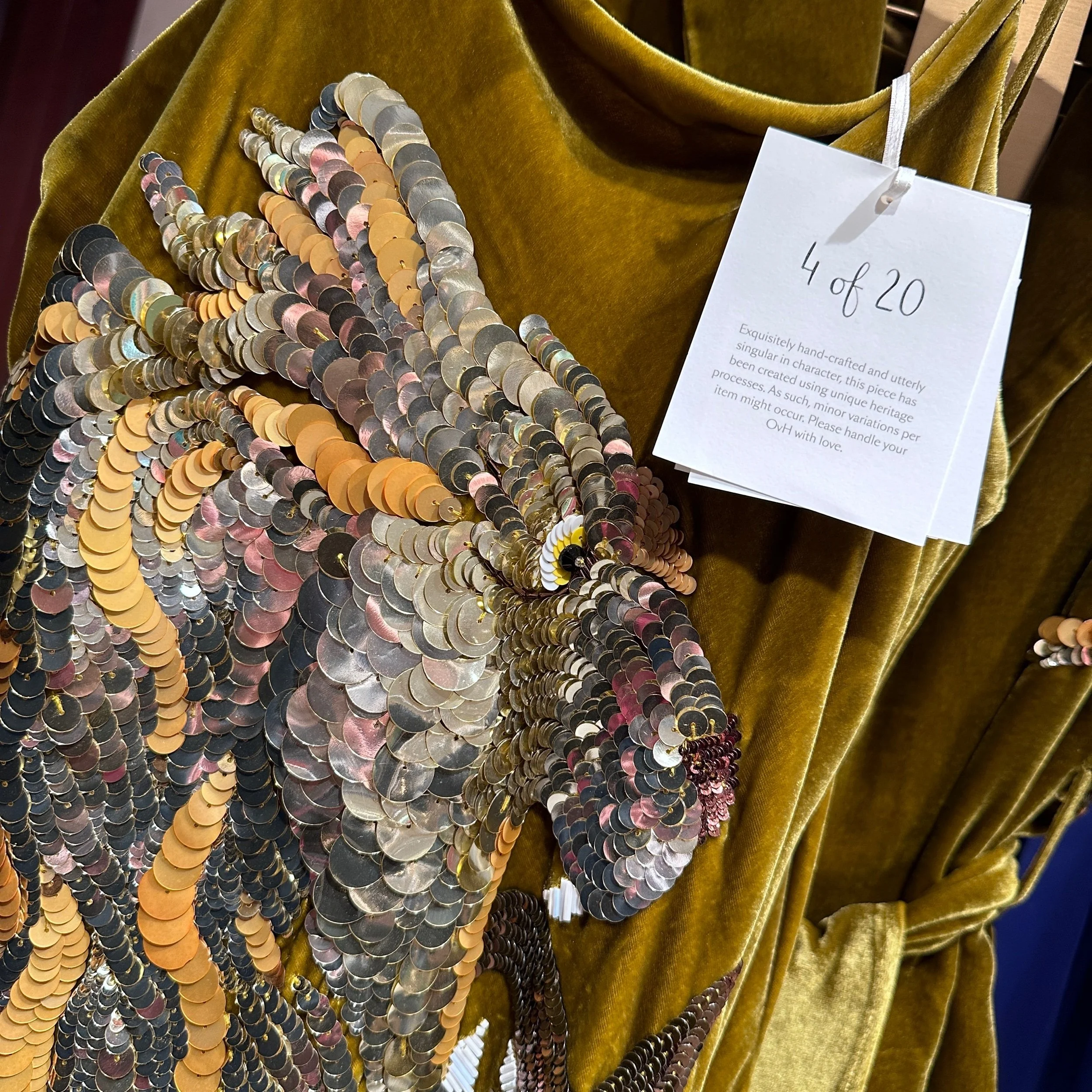 Close-up of swing tag lettered in black ink, and sequin embellishment on olivia von halle limited collection.