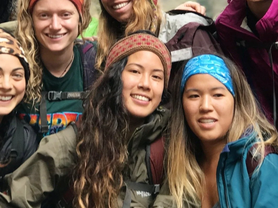 Group of five smiling women wearing outdoor gear and headbands, posing for a photo outdoors.