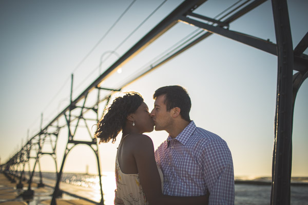 couple kissing on pier with windblown hair, backlight in golden hour, powerful connection