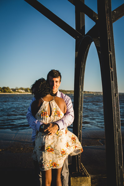 couple hugging on pier as light wraps around them and wind moves her dress