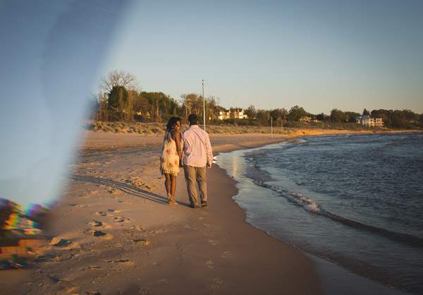 couple walking along beach as wife looks back, prism, golden hour 