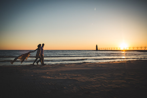 couple walking along beach in golden light, scarf flowing behind, movement, connection