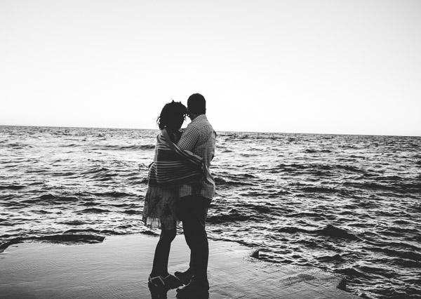 couple in warm embrace as they look out onto the water, black and white 