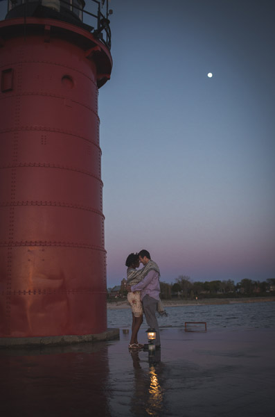 couple hugging in front of lighthouse with moon in background